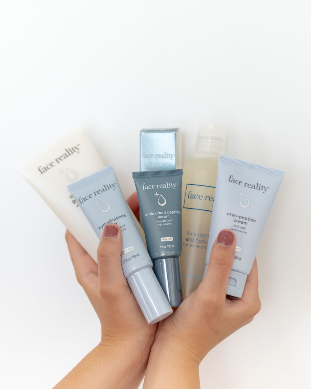 A person's hand holding five skincare products from Face Reality, including serums and creams, with a white background.