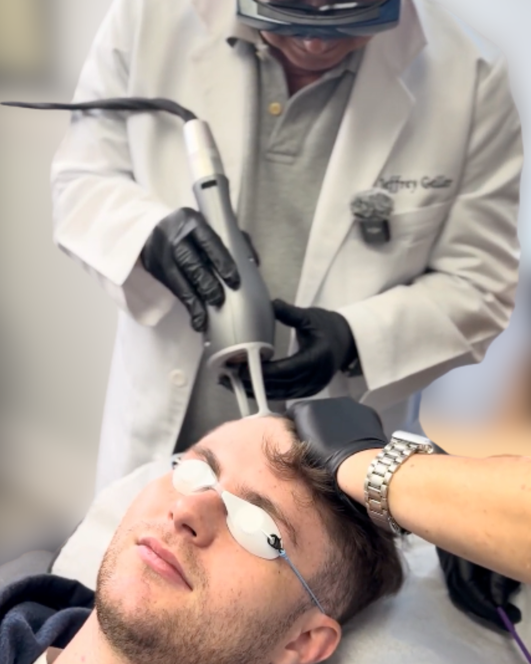 A person receiving a dental or cosmetic procedure using a laser device, with the patient lying down and protective eye goggles on.