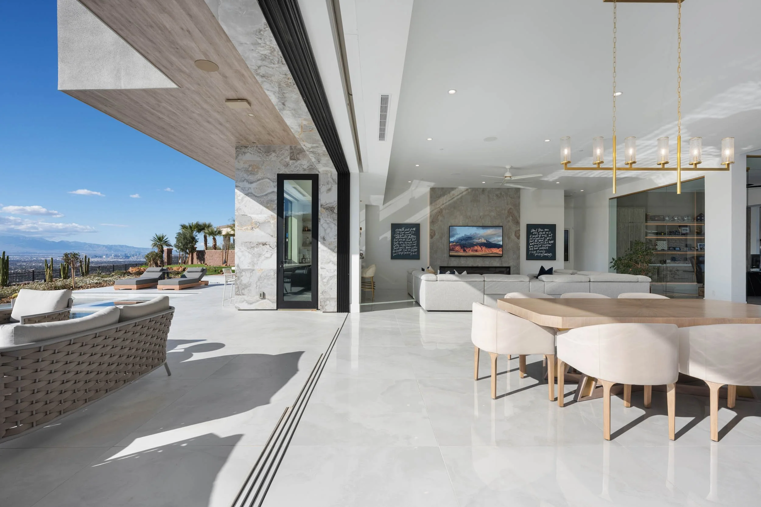 Modern open-concept living and dining area with large sliding glass doors leading to an outdoor patio with lounge chairs and desert landscape.
