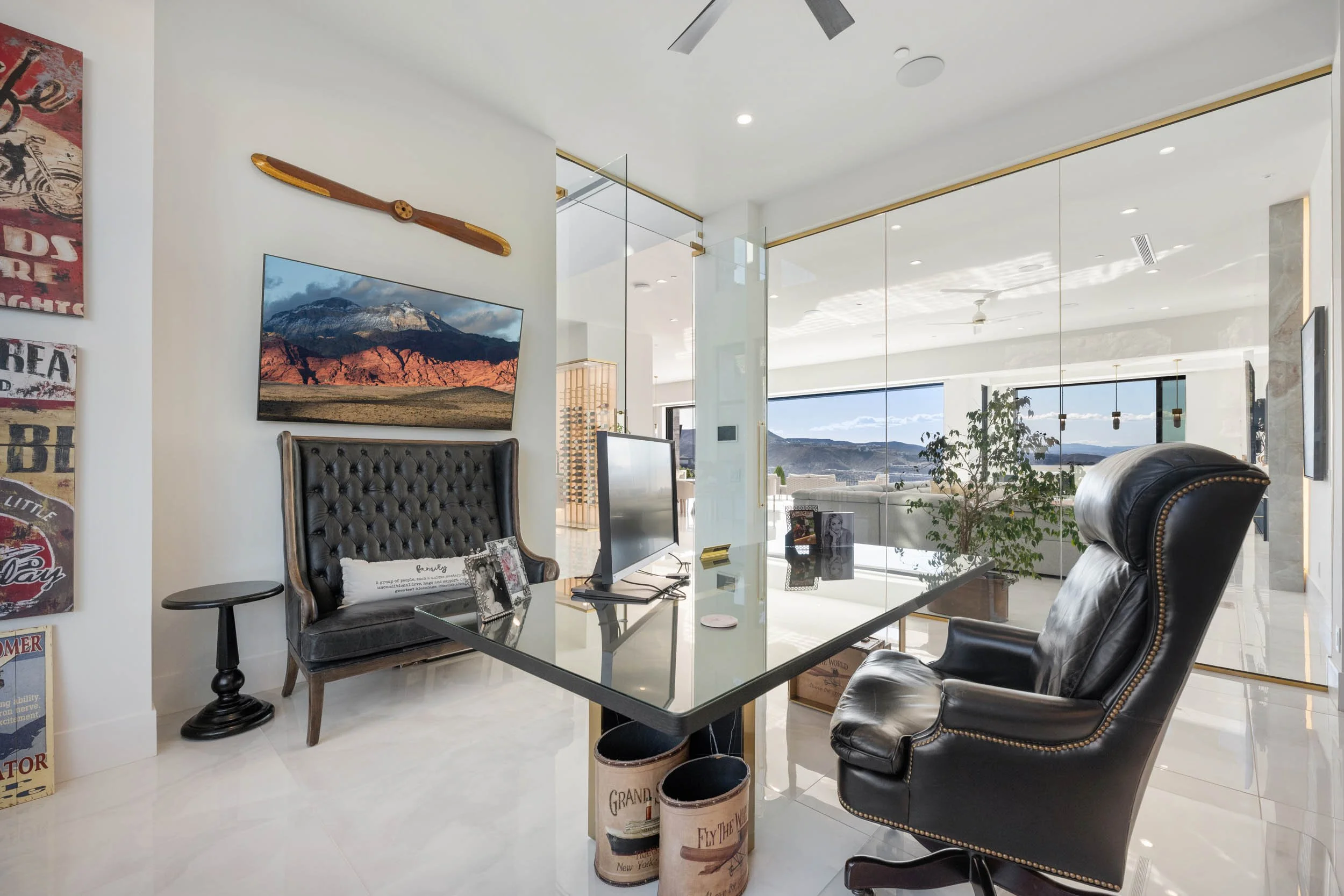 Modern office with glass walls, black leather chairs, a glass desk, and a large window view of mountains and landscape.