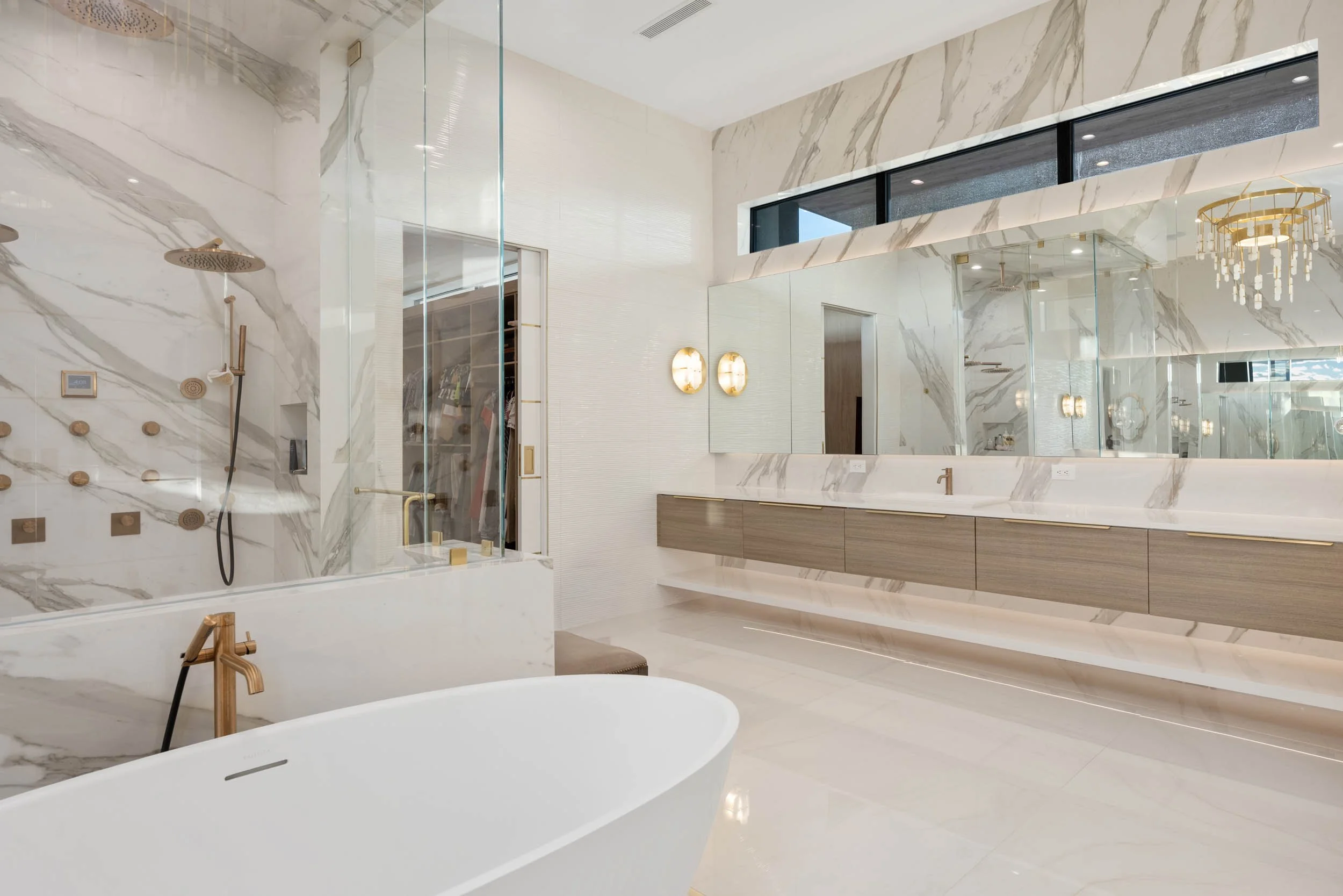Luxury bathroom with marble walls and floors, large mirror, freestanding bathtub, double vanity, and walk-in shower with multiple showerheads.