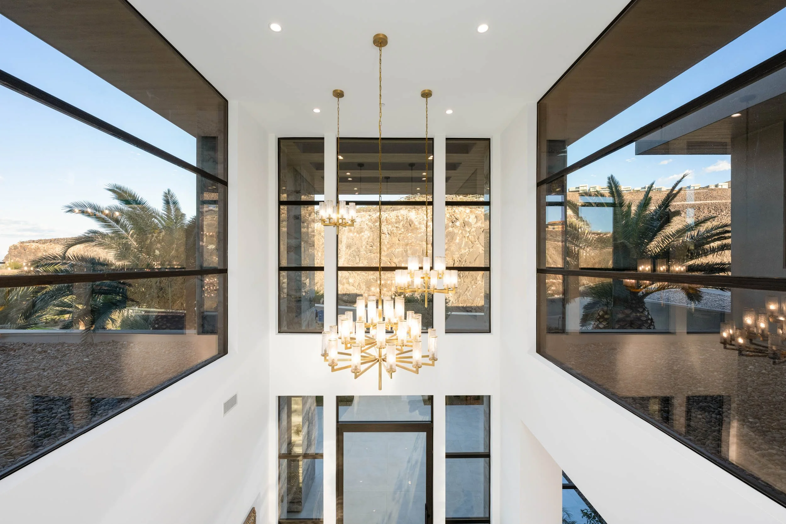 Interior view of a modern house with a double staircase, large windows, and a chandelier.