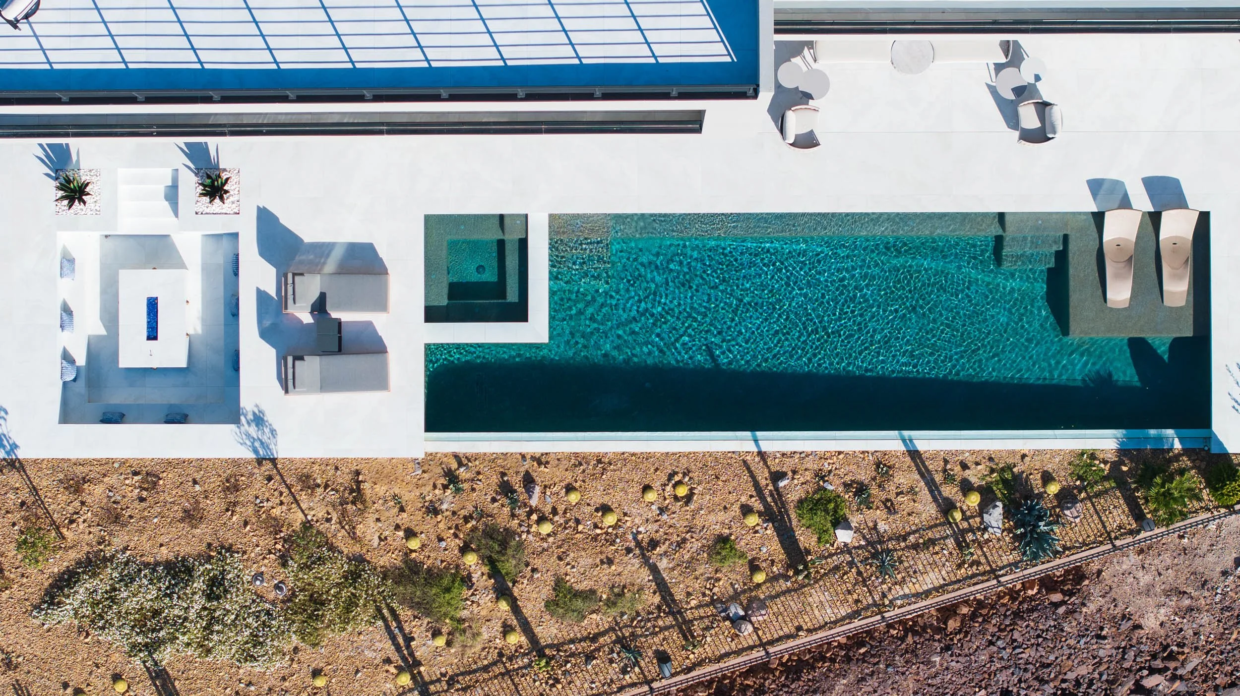 Aerial view of a modern rooftop swimming pool area with lounge chairs, umbrellas, and desert landscaping.