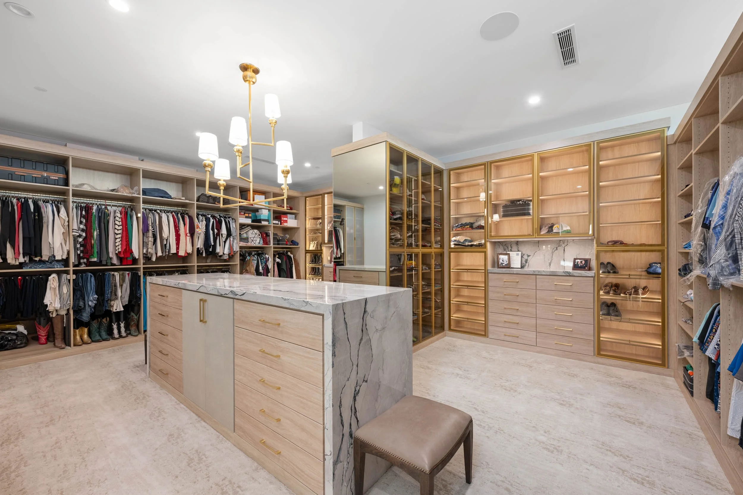 Modern walk-in closet with built-in shelves, drawers, and hanging space, featuring a marble-topped island and a chandelier.