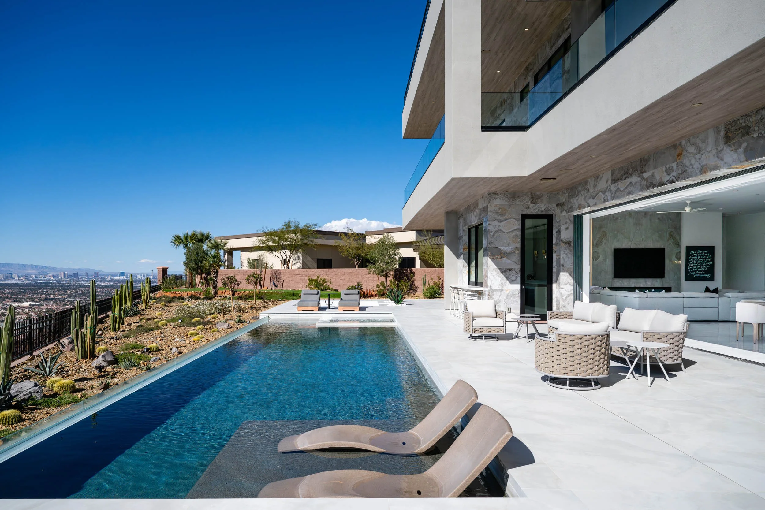 Modern house with a swimming pool, outdoor seating, and views of a cityscape and desert landscape under a clear blue sky.