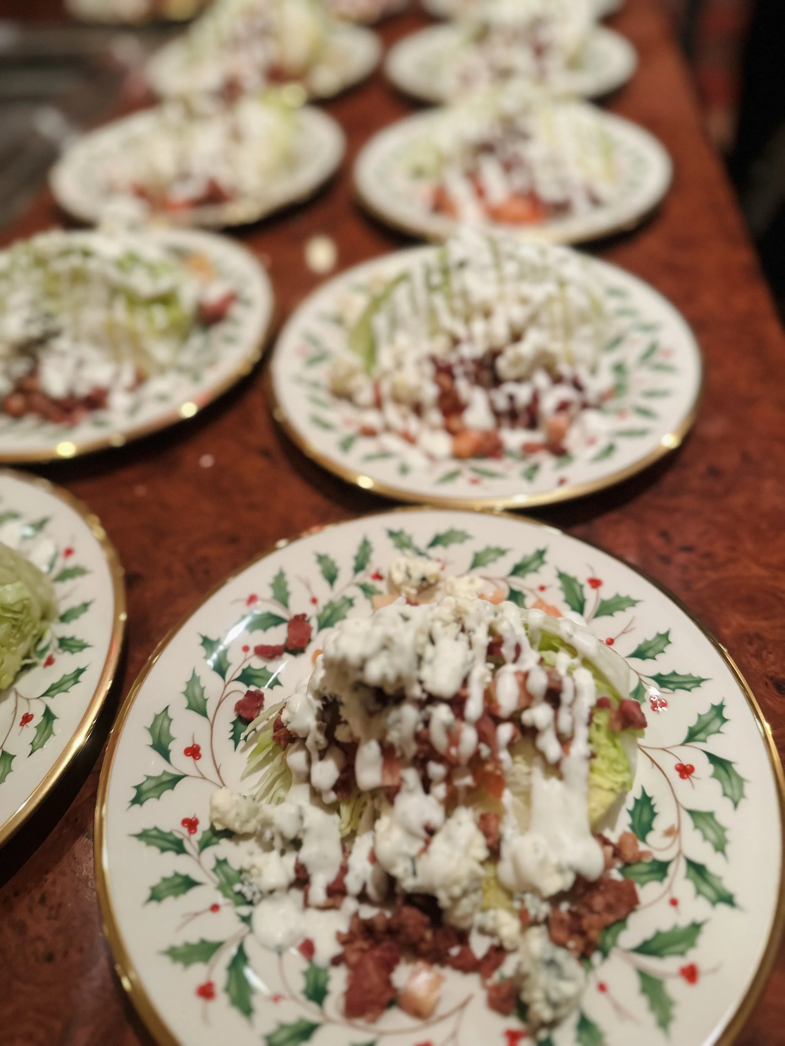 A plate of salad with lettuce, tomatoes, crumbled cheese, bacon bits, and a drizzle of dressing on a festive holiday plate with holly and berries design.