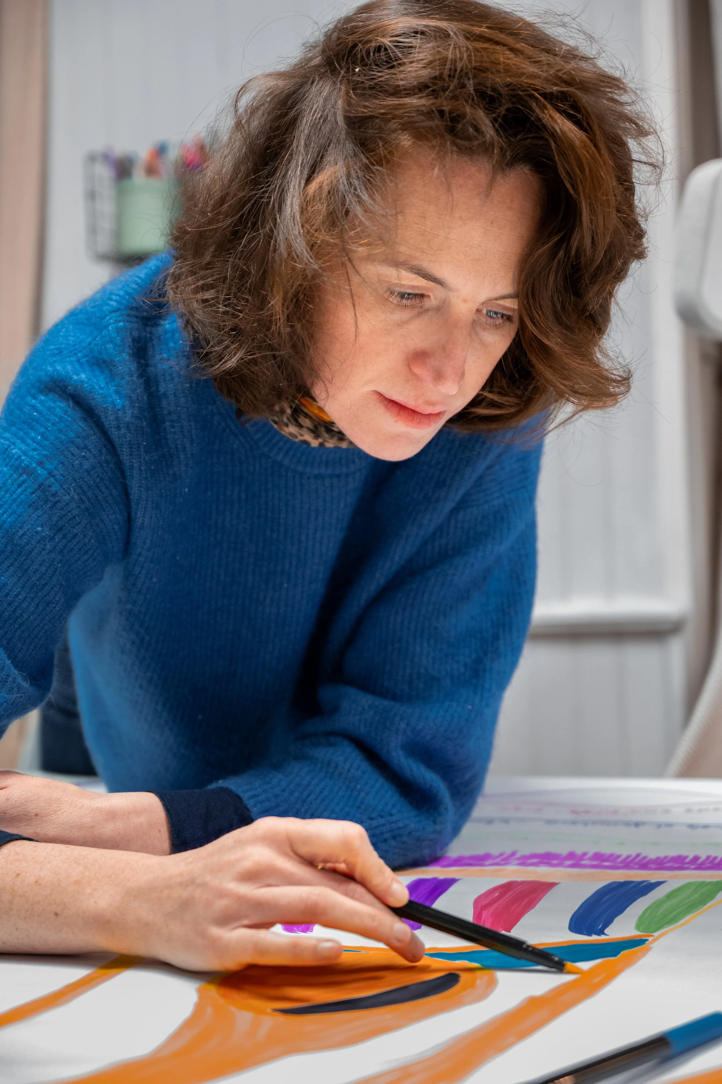 Femme concentrée qui peint un tableau avec des couleurs vives et des pinceaux.