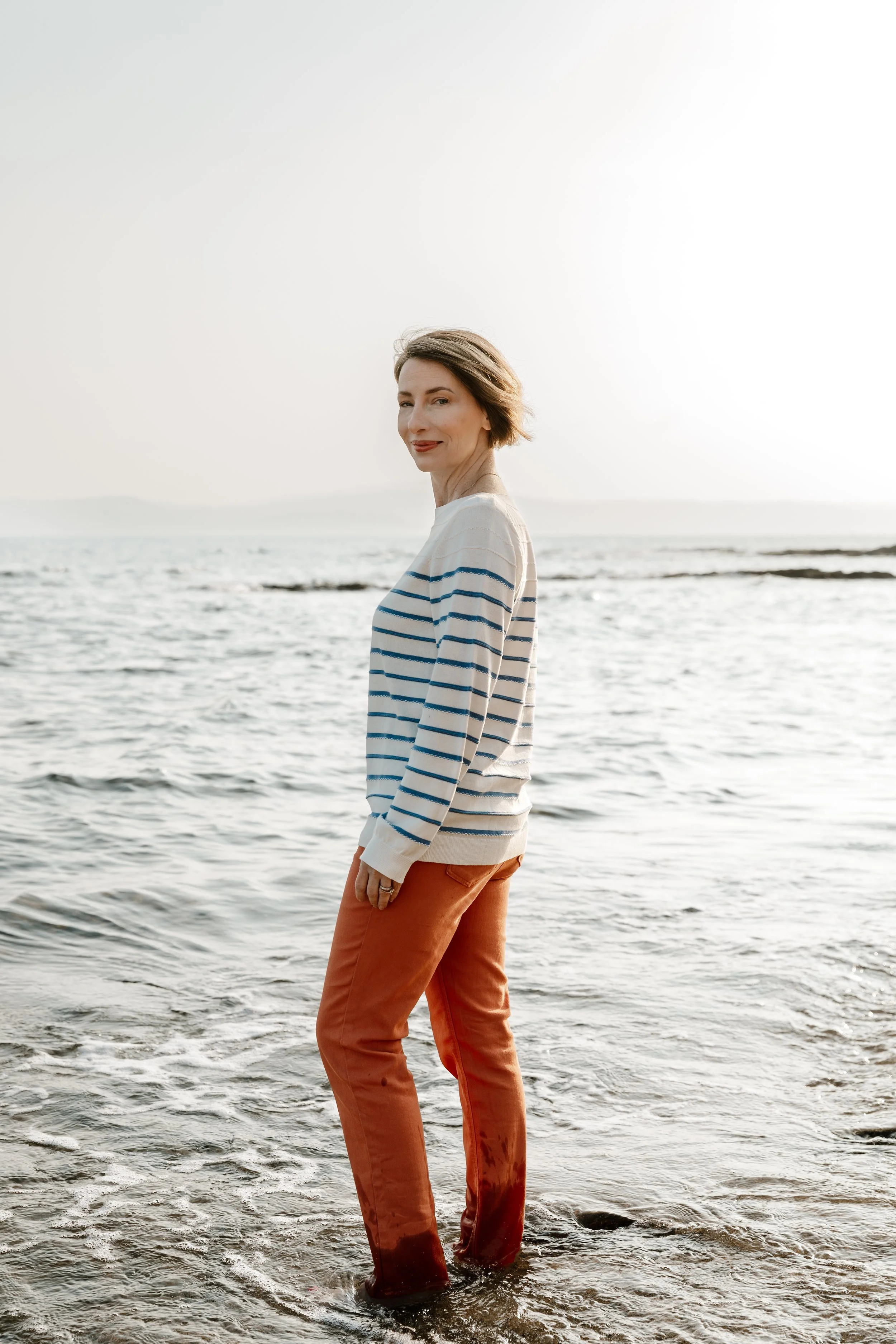 RaChel Benyair standing in the ocean at the beach, looking at the camera with a smile, during sunset.