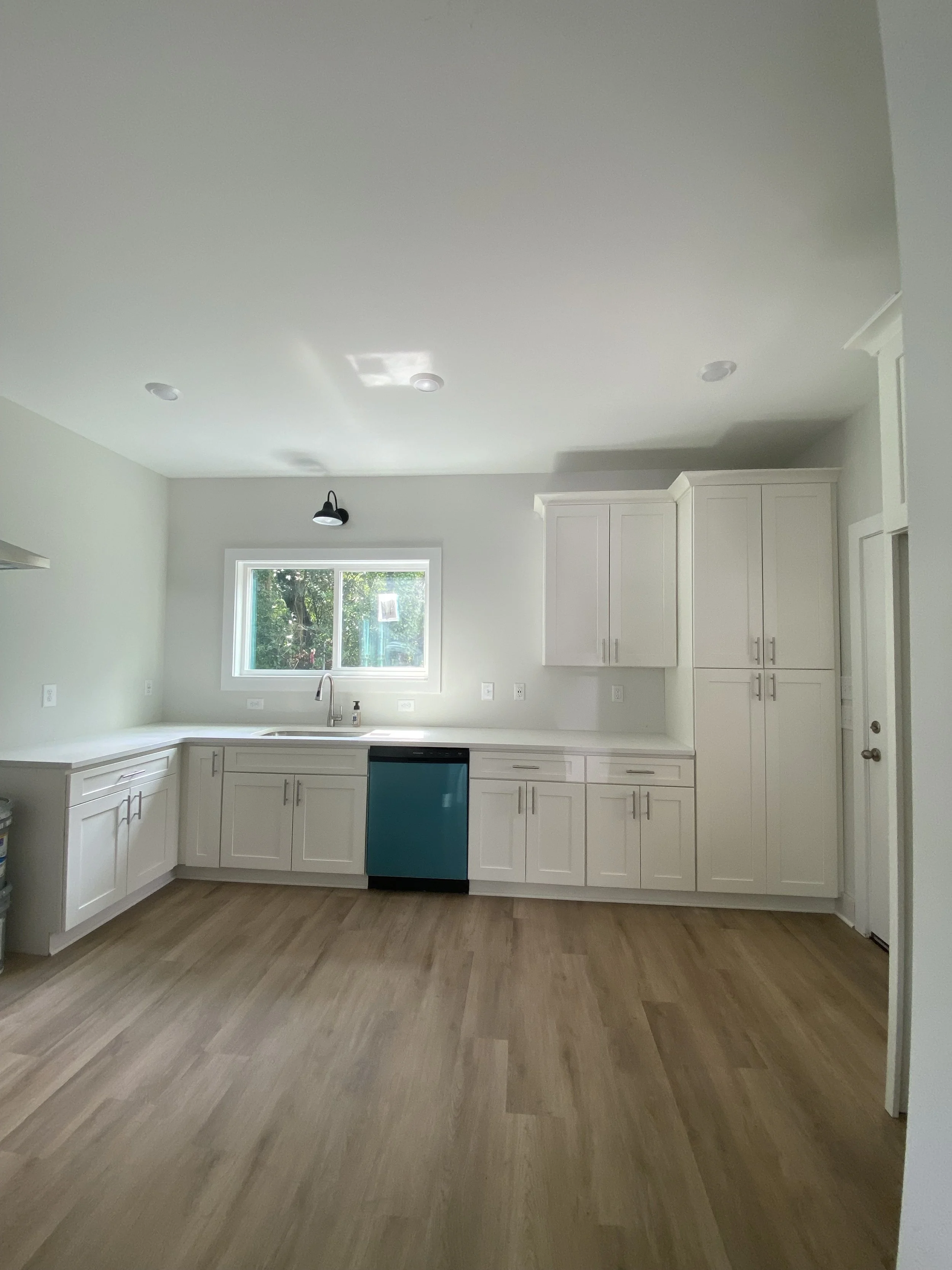 Modern kitchen with white cabinets, a window above the sink, a blue dishwasher, and wood flooring.