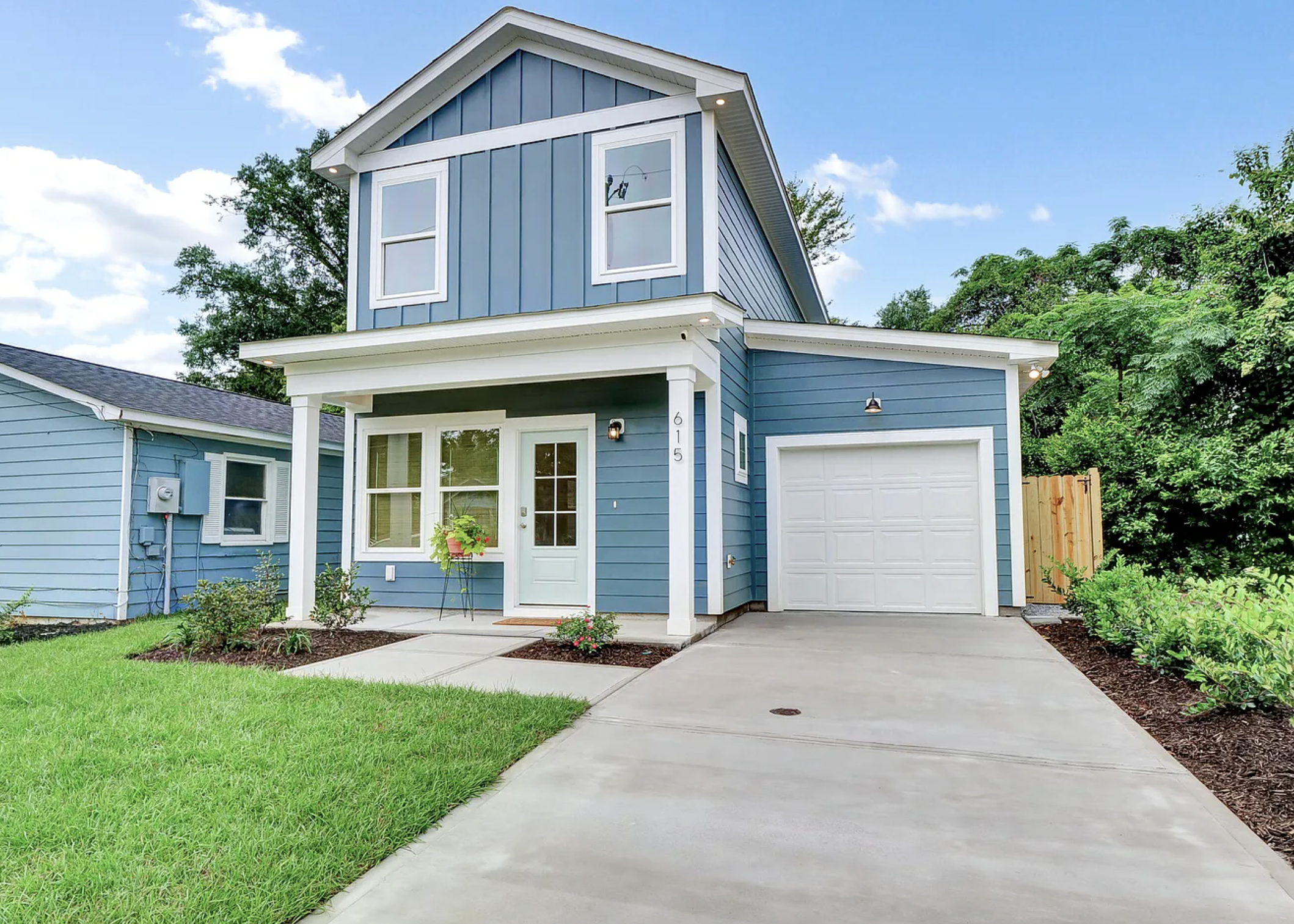 Front view of a modern blue two-story house with a white garage door, a front porch, and a well-maintained lawn under a partly cloudy sky.