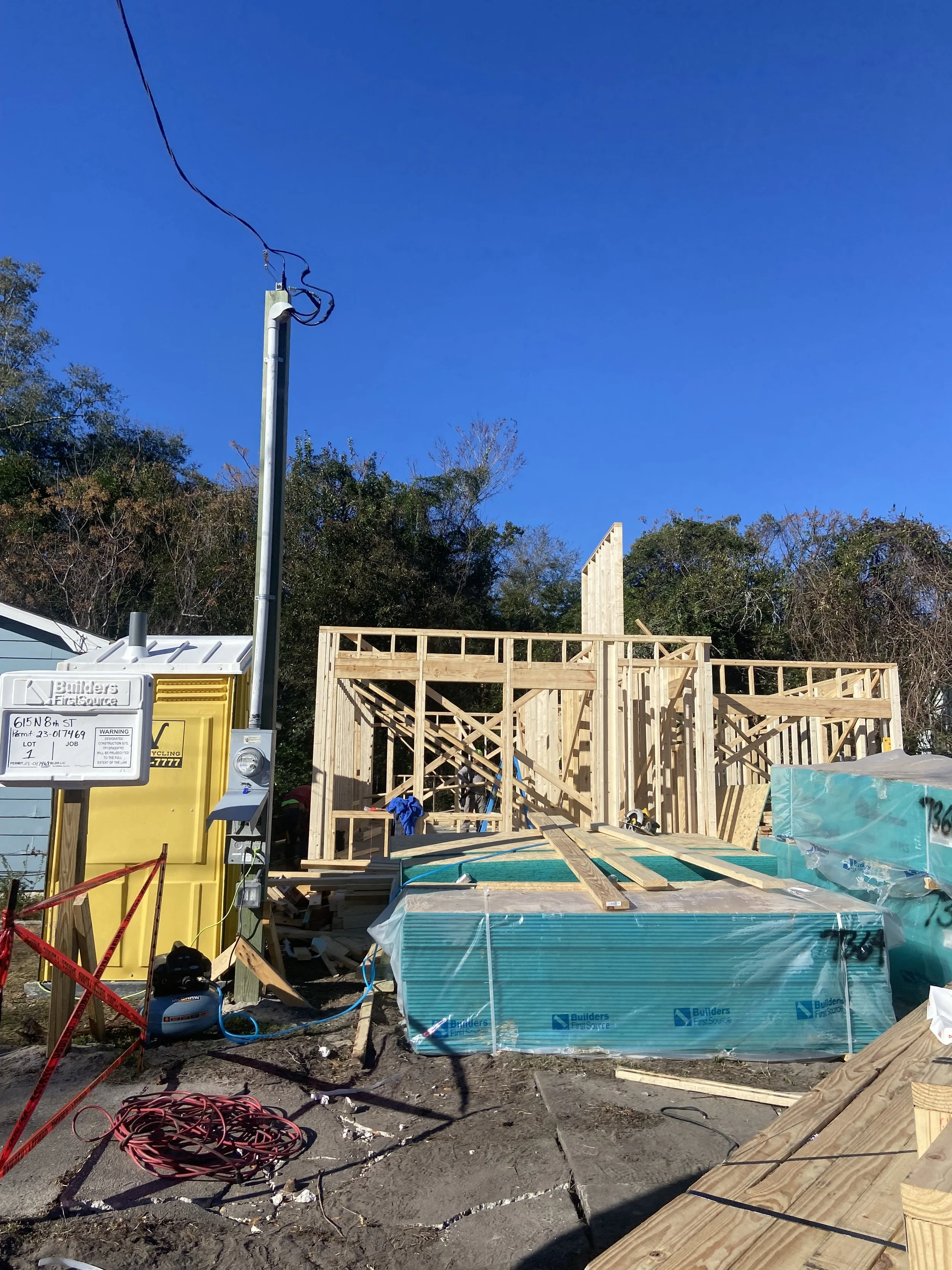 Construction site with wooden framing for a building, building materials, and a power pole against a blue sky.