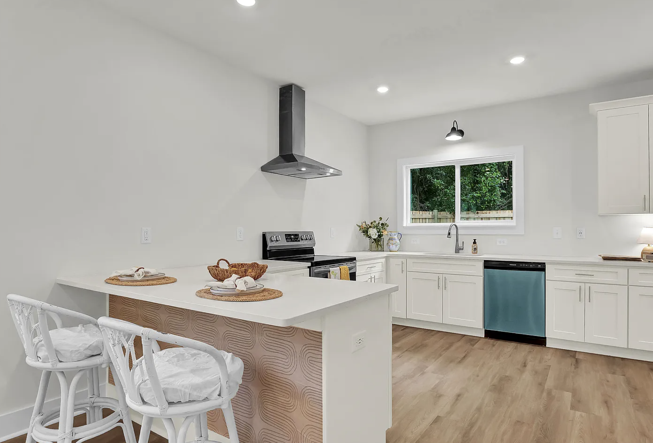 Modern kitchen with white cabinets, black stove, blue dishwasher, and wood flooring, featuring a window over the sink and decorative items on the counter.