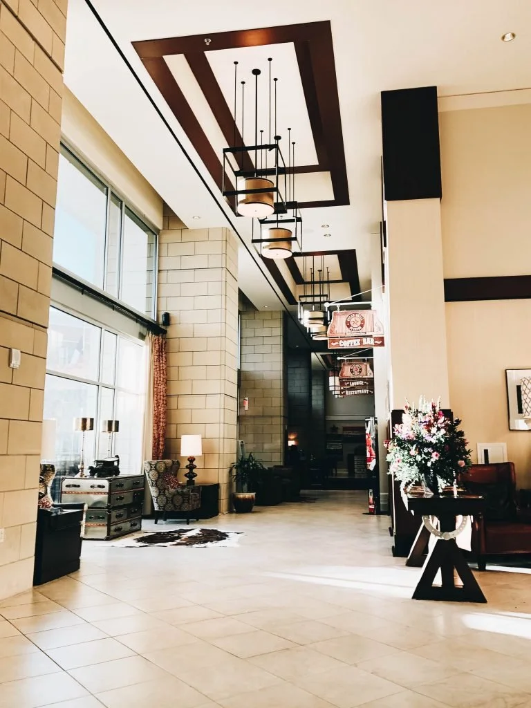 Lobby with large windows, high ceilings, modern lighting fixtures, armchairs, a floral arrangement on a table, and a cowhide rug.