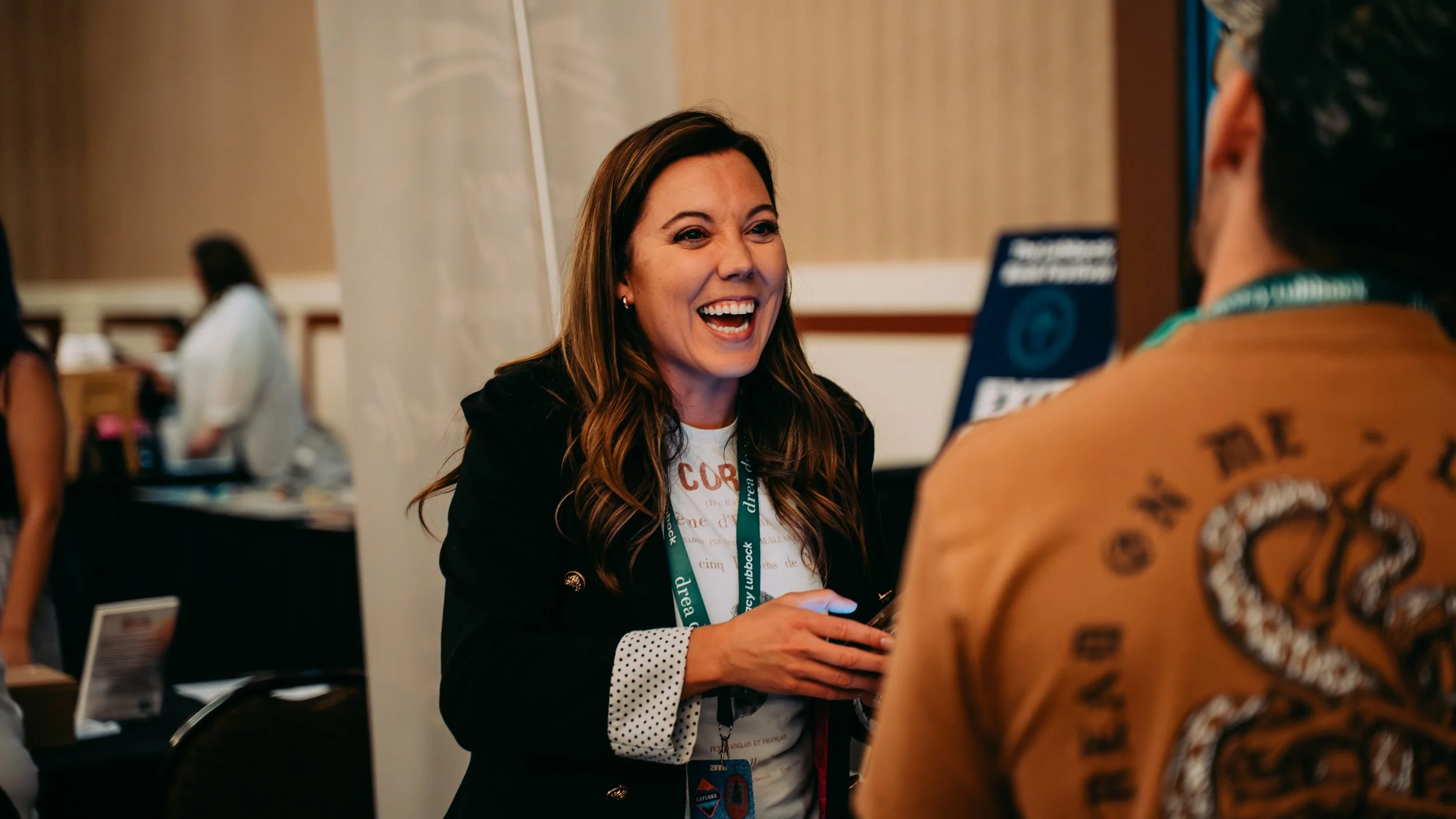 Woman smiling and talking to another person at a conference or event, with a badge featuring a snake patch on their clothing.