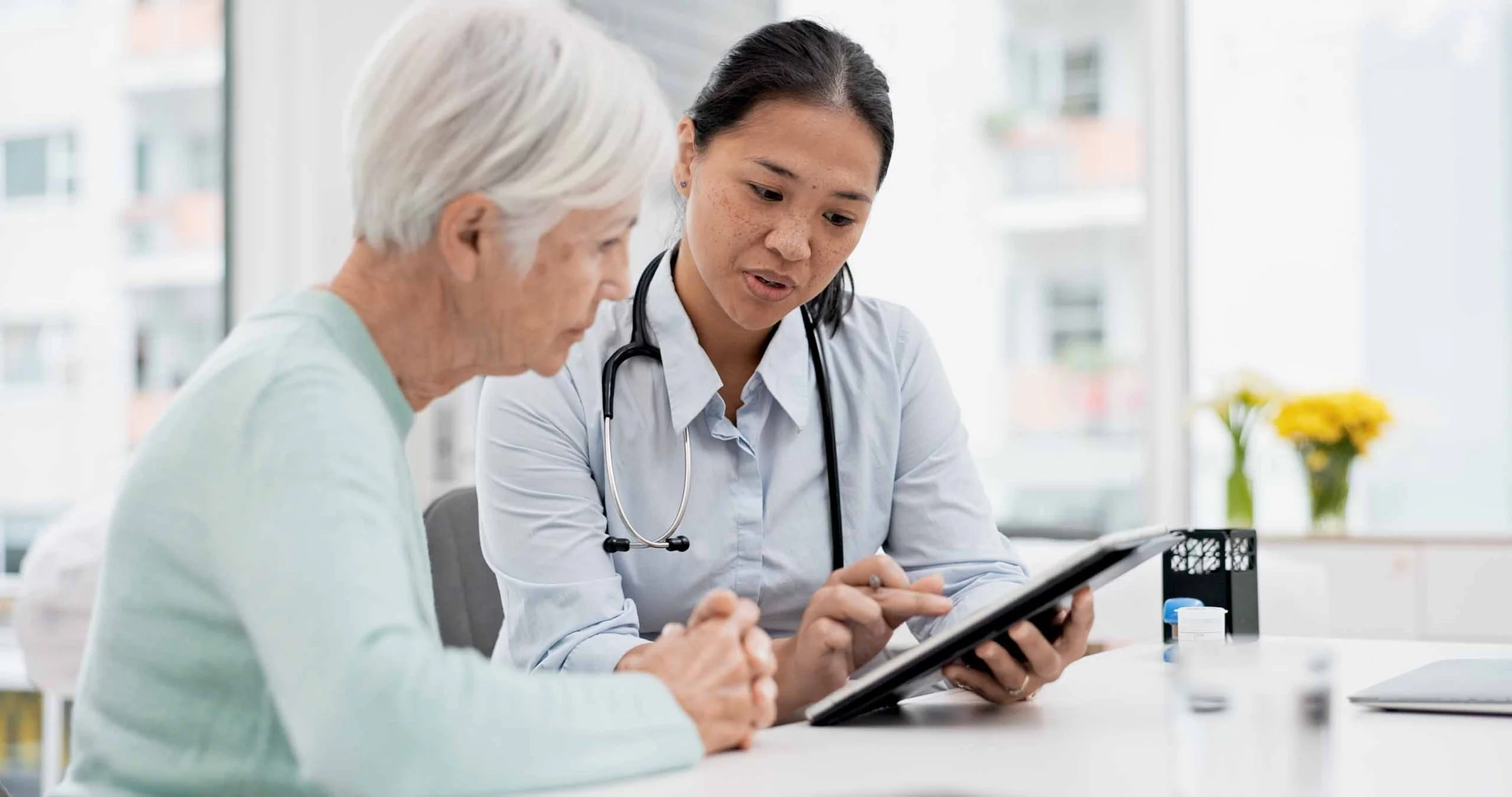A healthcare professional showing a tablet to an elderly woman during a consultation in a medical office.