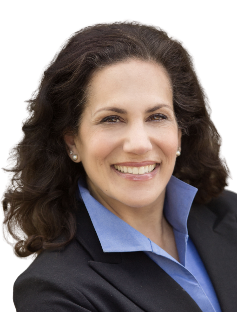 A woman with shoulder-length dark brunette hair, smiling, wearing a black blazer over a blue collared shirt, and pearl earrings.