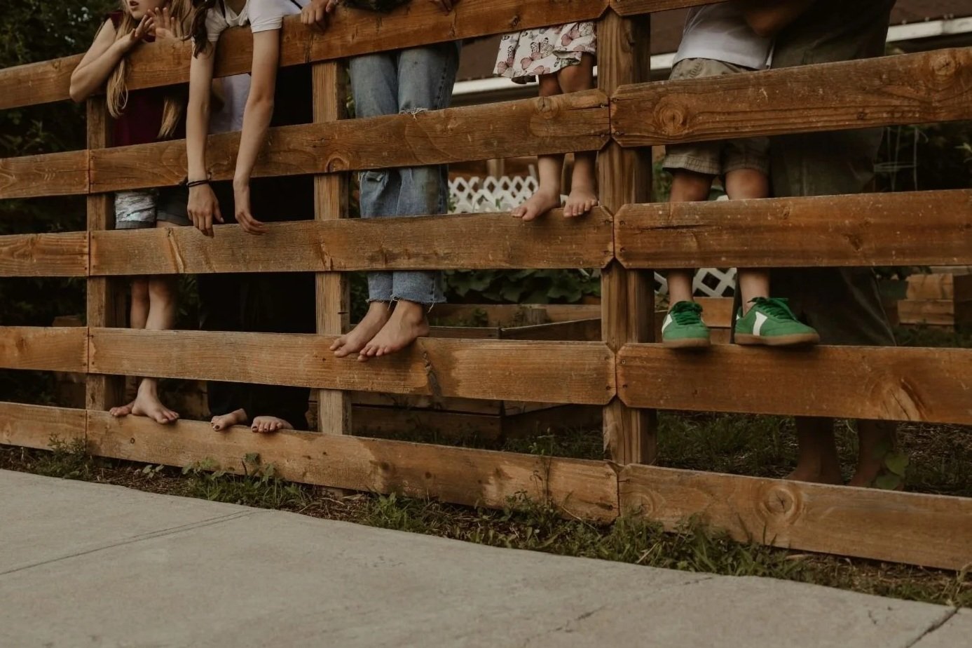 Children standing behind a wooden fence, showing only their legs and feet.