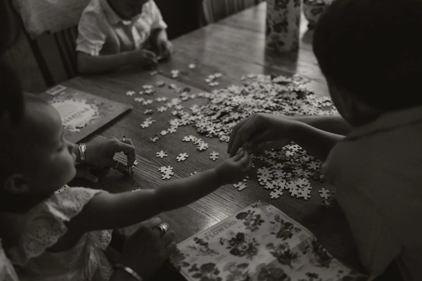 People working on assembling a jigsaw puzzle on a wooden table.
