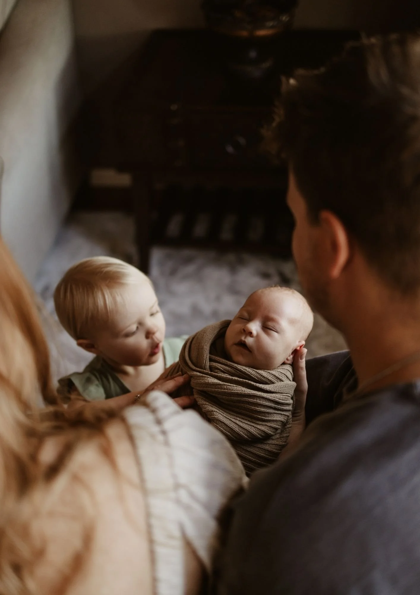 A family holding a newborn baby and a toddler in a cozy indoor setting.