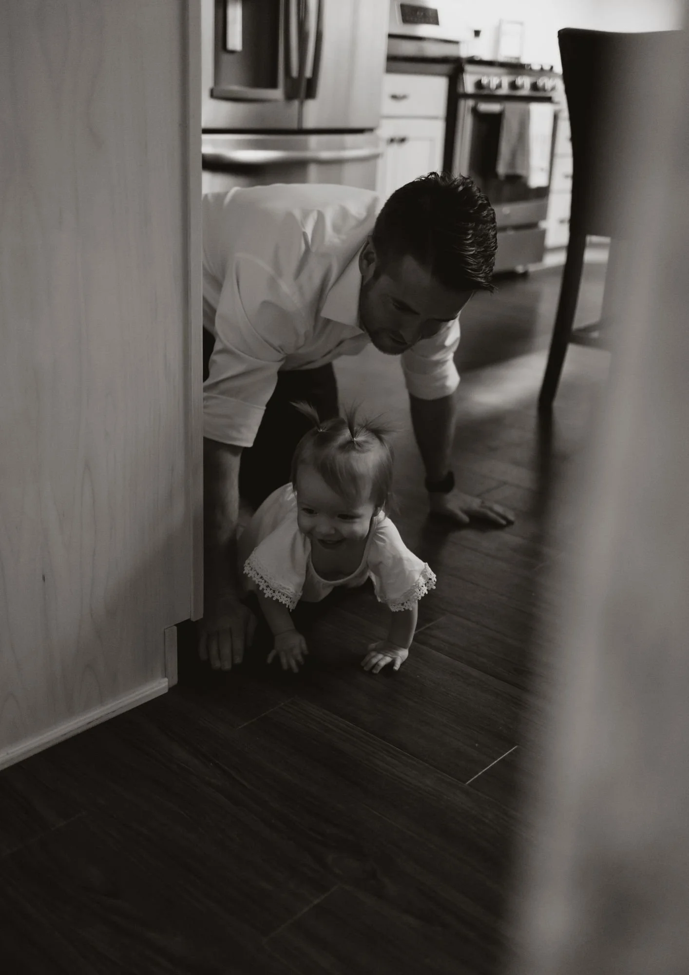 Man and young girl crawling on the kitchen floor, smiling at each other.
