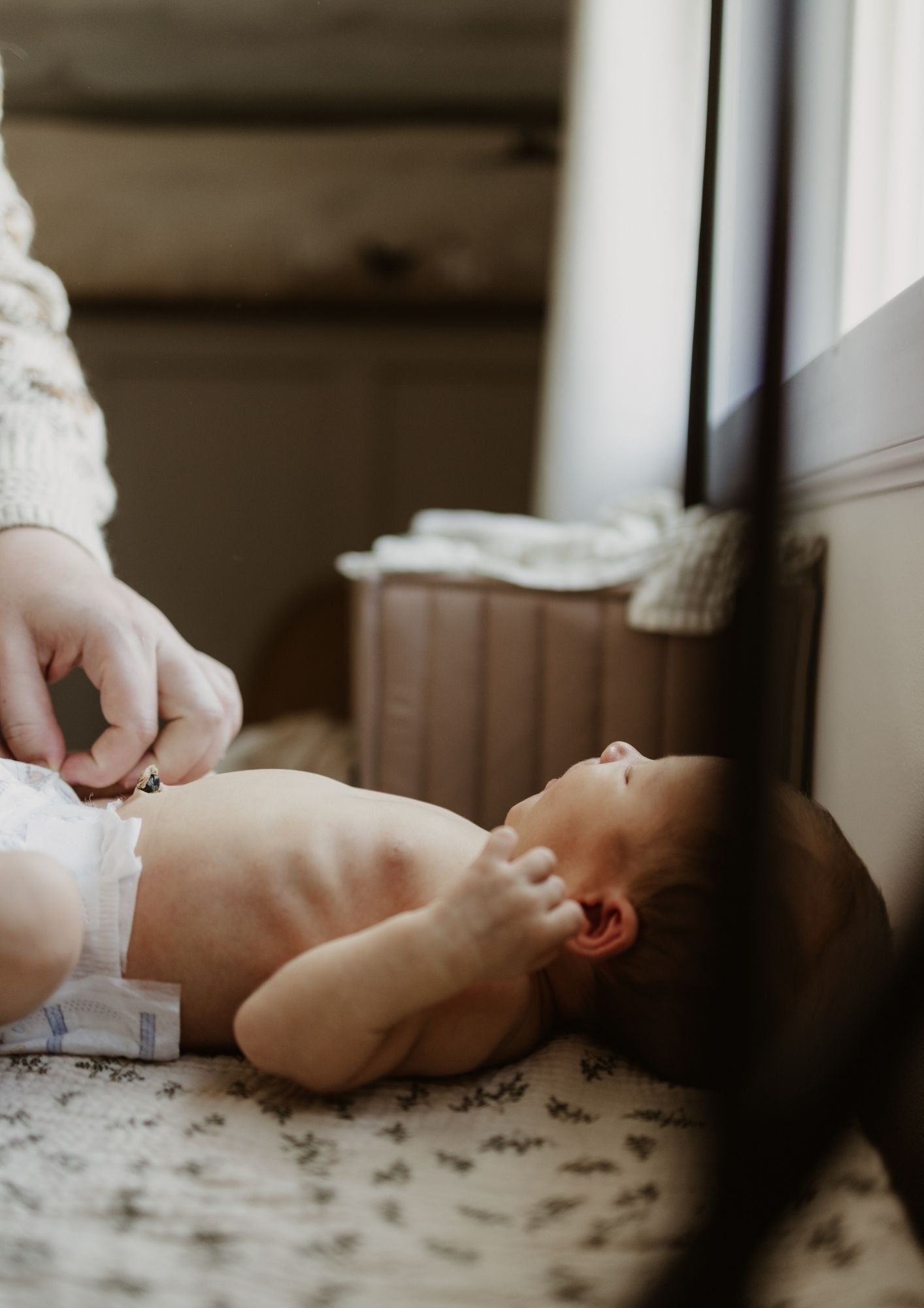 A young child lying on a bed, looking to the side, with an adult's hand changing their diaper.