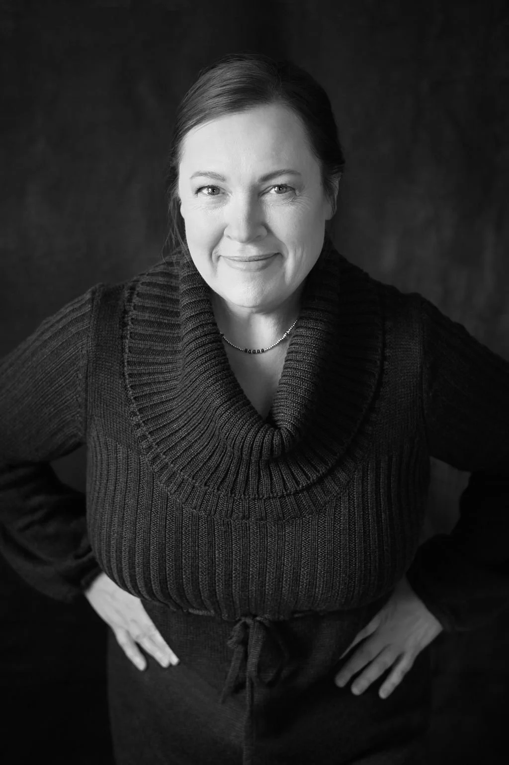 Black and white portrait of a woman with straight hair, wearing a chunky knit turtleneck sweater, smiling at the camera.