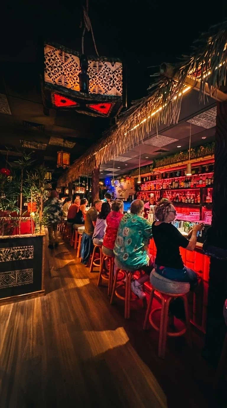 Guests relax at the tropical cocktail bar inside Spork Island Trading Company, Pittsburgh's immersive island-inspired restaurant featuring handcrafted cocktails, flavorful small plates, and authentic tiki décor.