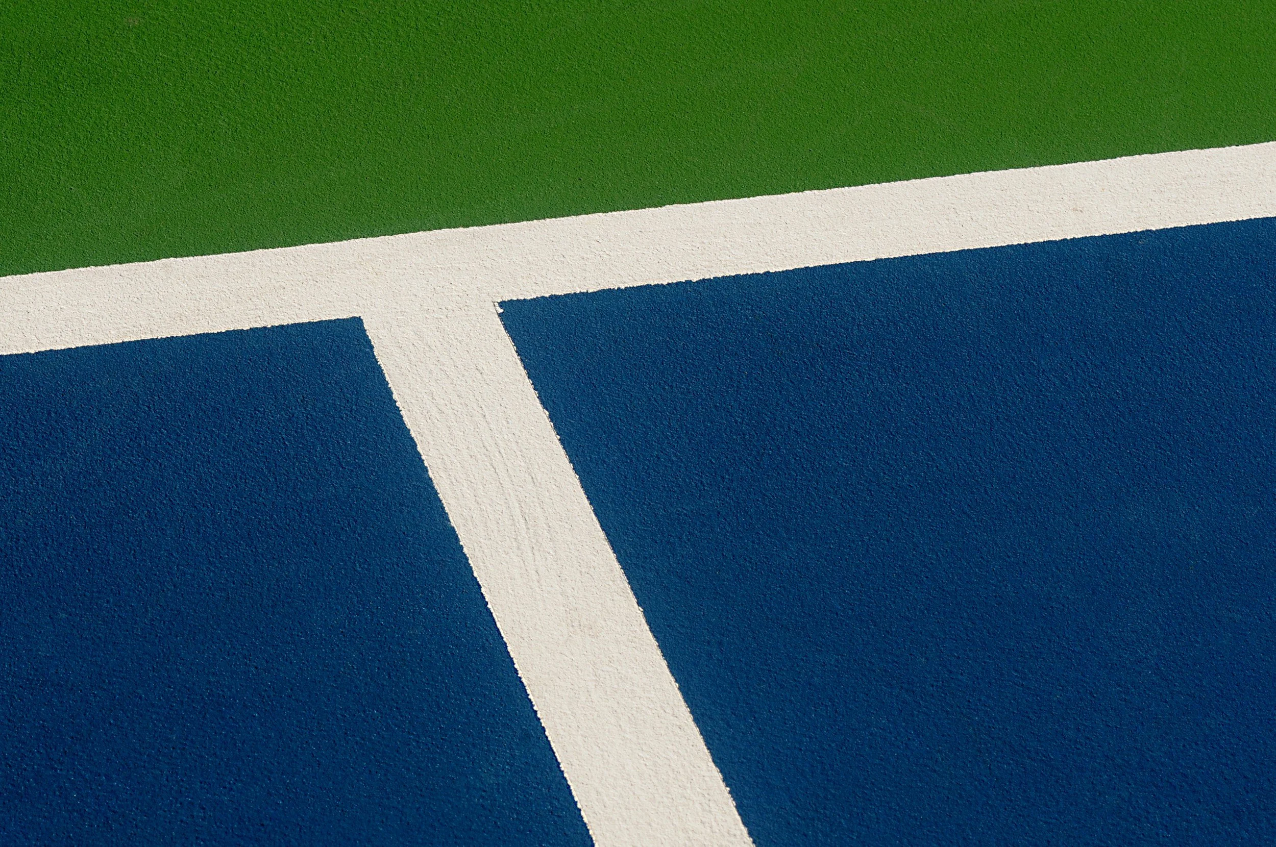 Close-up view of a tennis court surface showing green, white, and blue court lines.