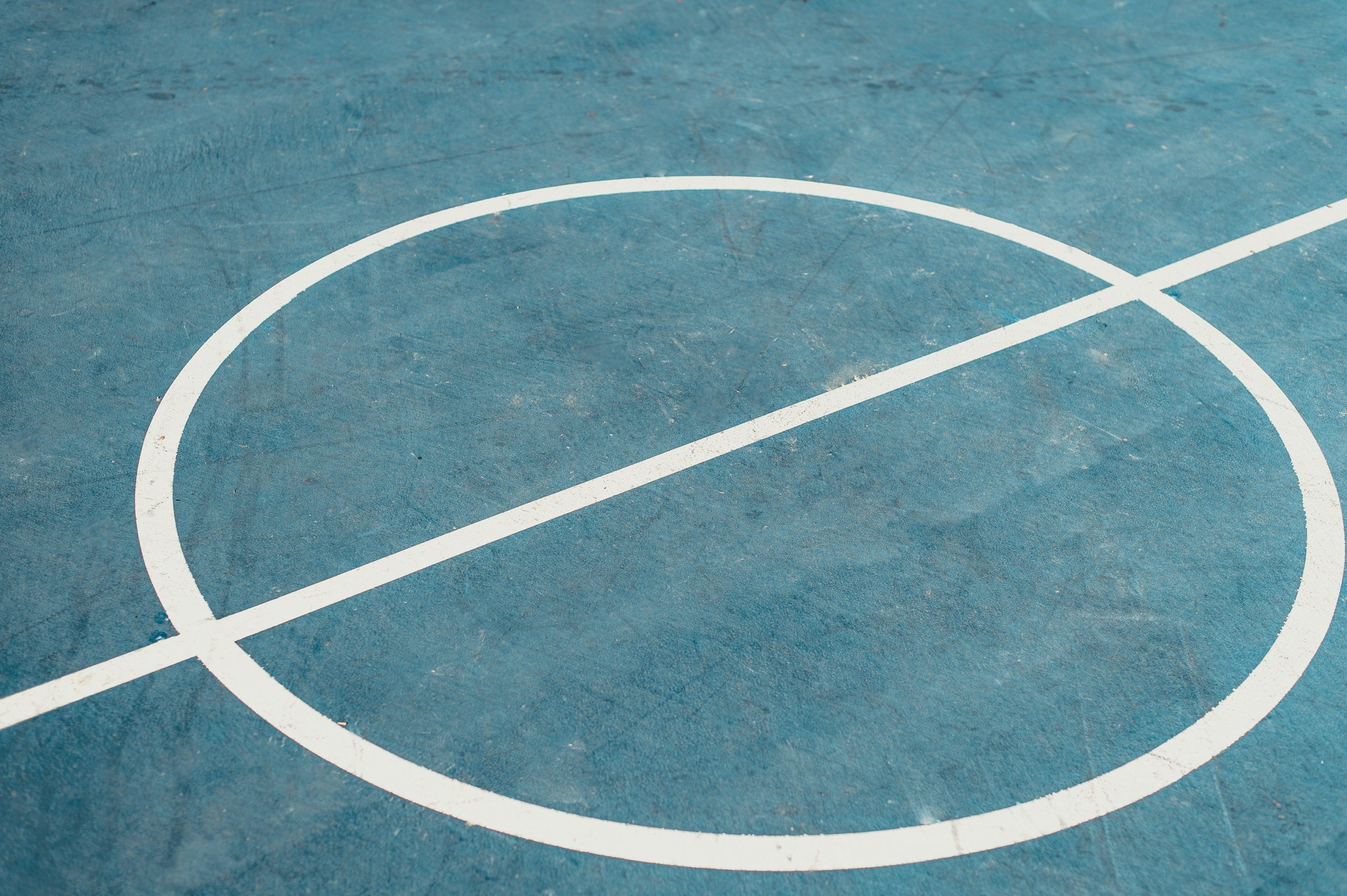 Close-up of a blue outdoor sports court with white painted lines and a circular marking.