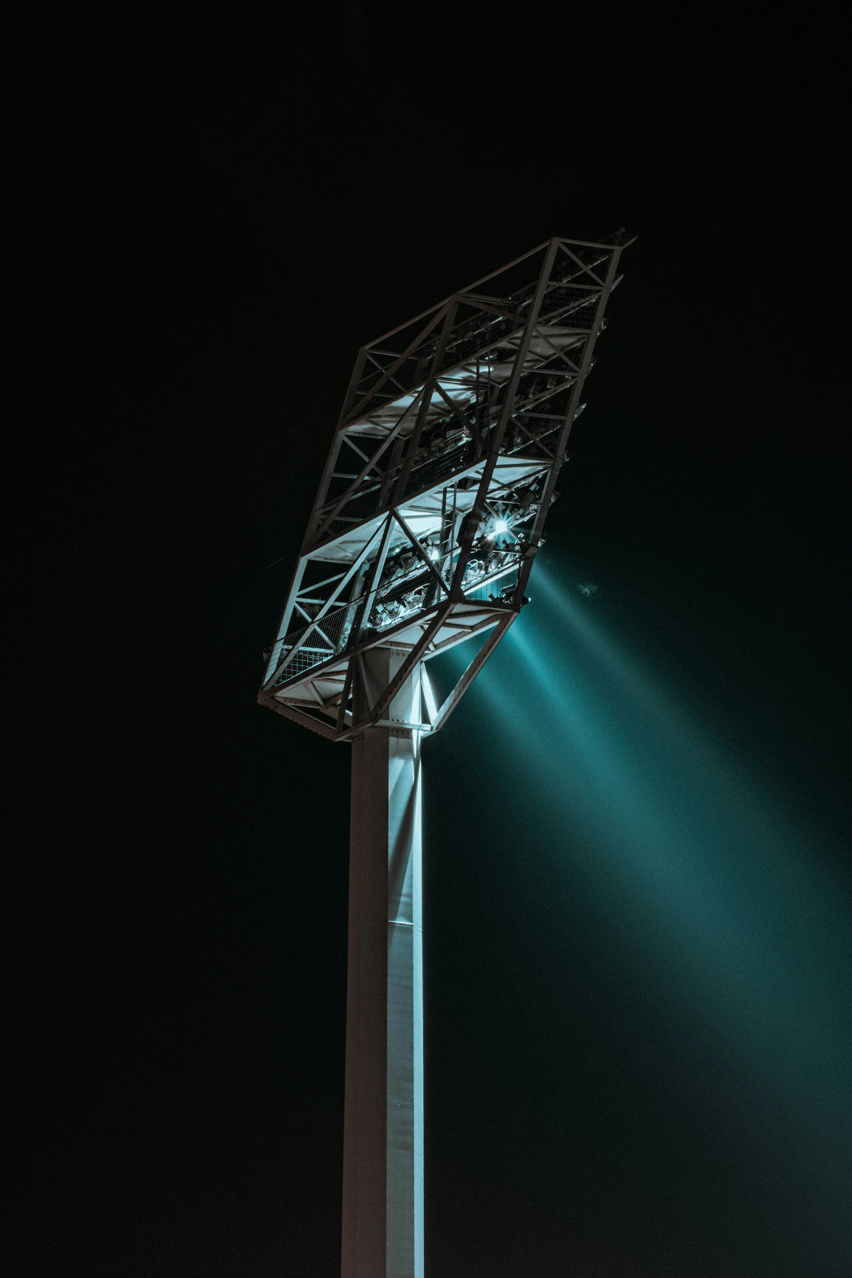 A tall stadium light tower illuminated at night, with multiple bright beams shining outward.