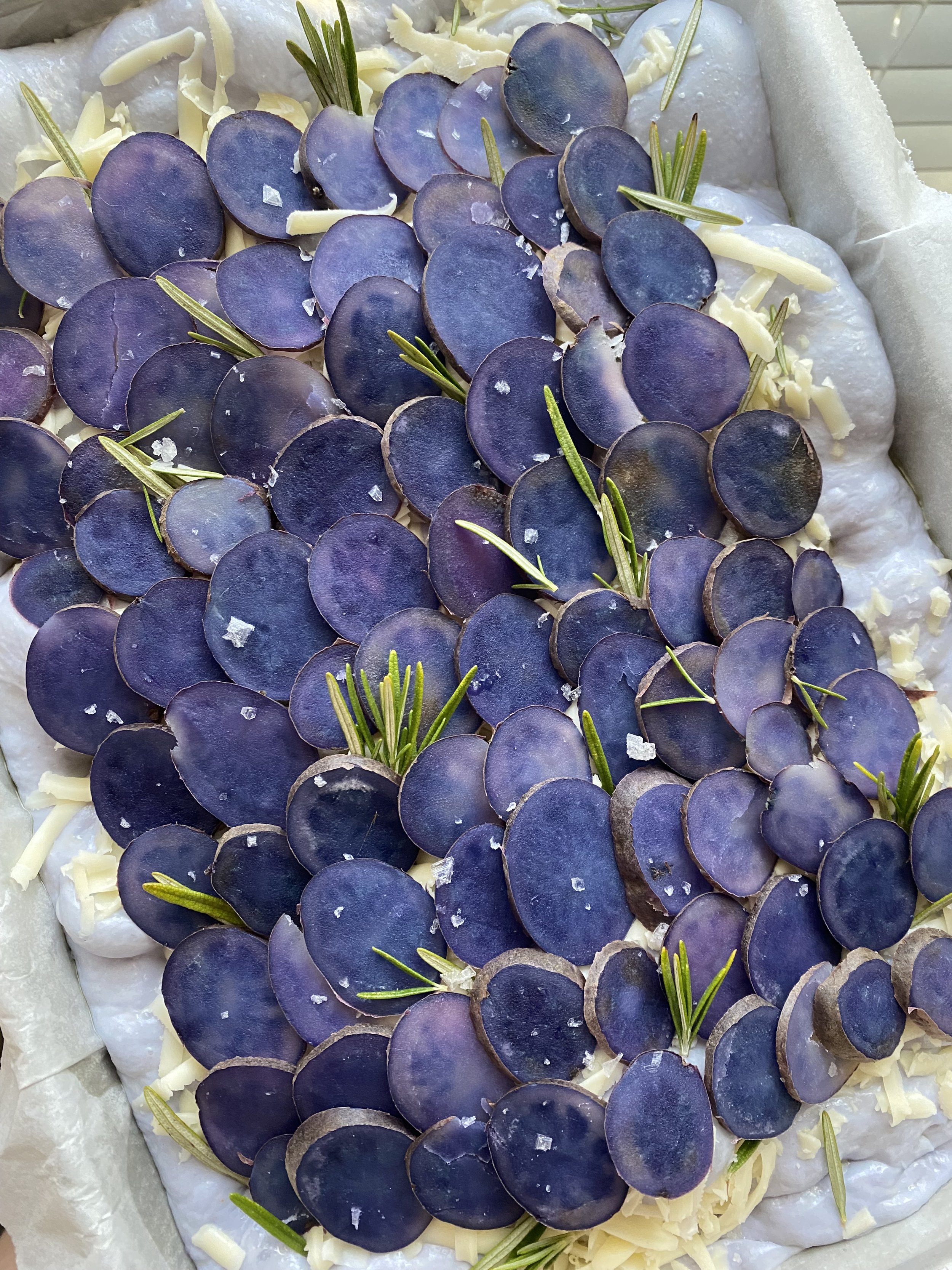 Purple potato focaccia with mozzarella and sprigs of rosemary on a light-colored surface.