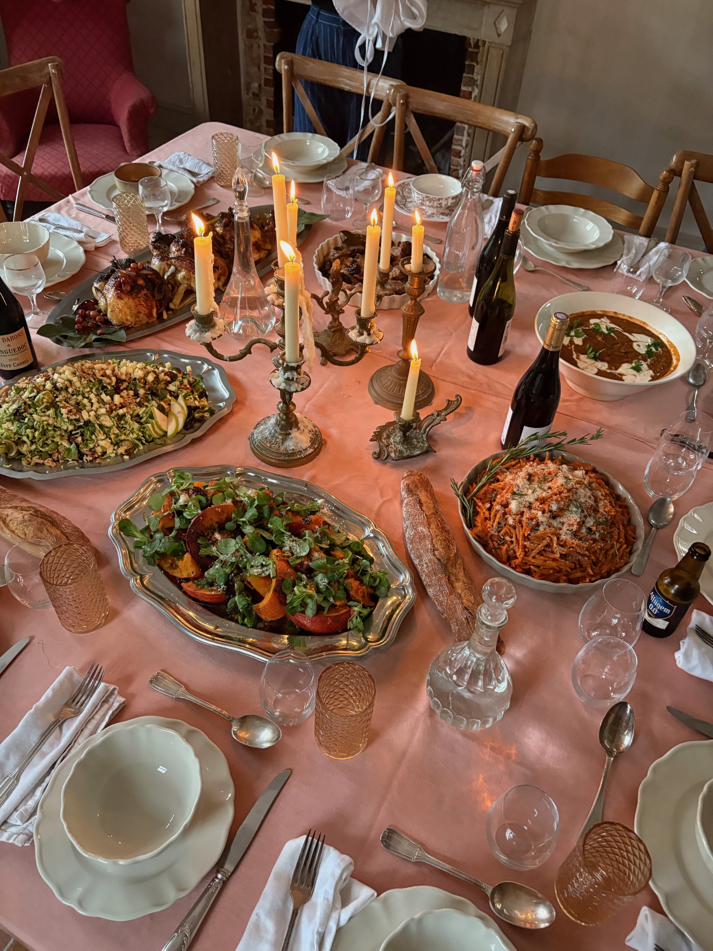 A dining table set for a meal with multiple dishes, including roasted chicken, pasta, salad, and bread, decorated with candelabra and surrounded by empty plates and glasses.