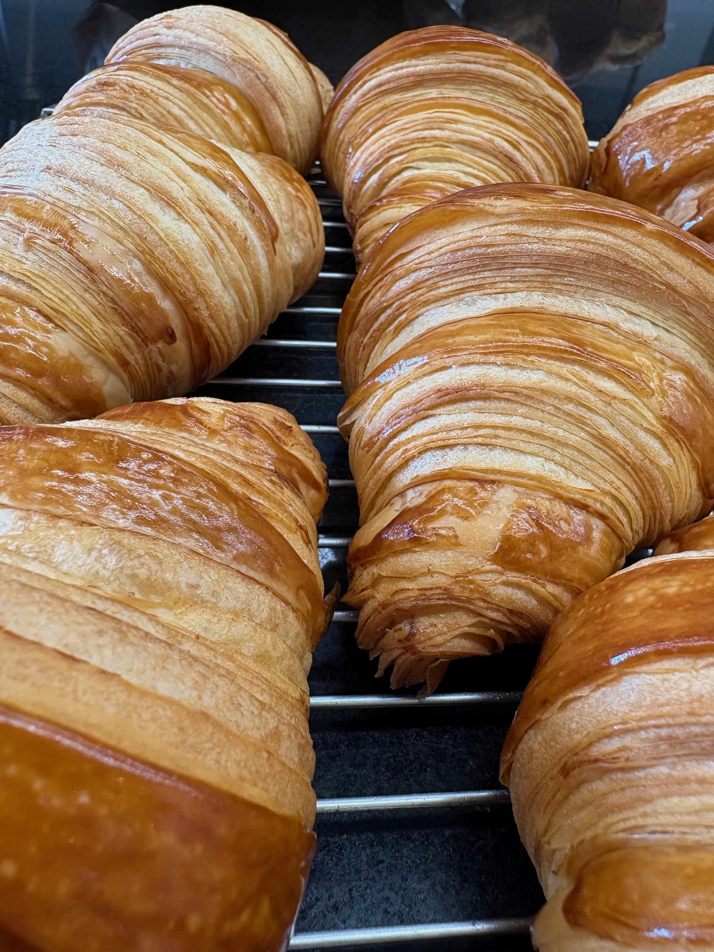 Multiple golden-brown croissants cooling on a wire rack.