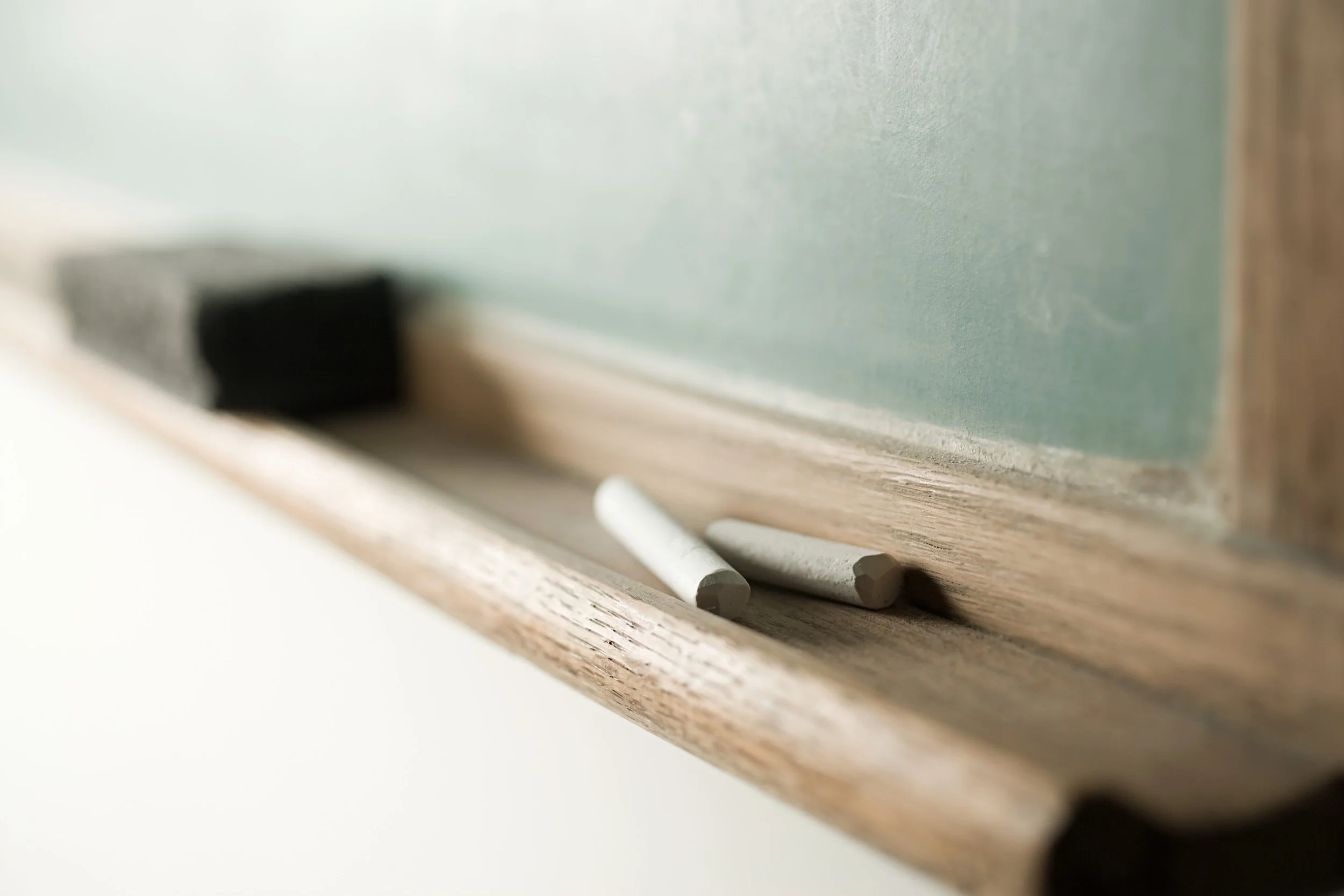 Close-up of chalkboard chalks on a wooden ledge, with part of a chalkboard in the background.