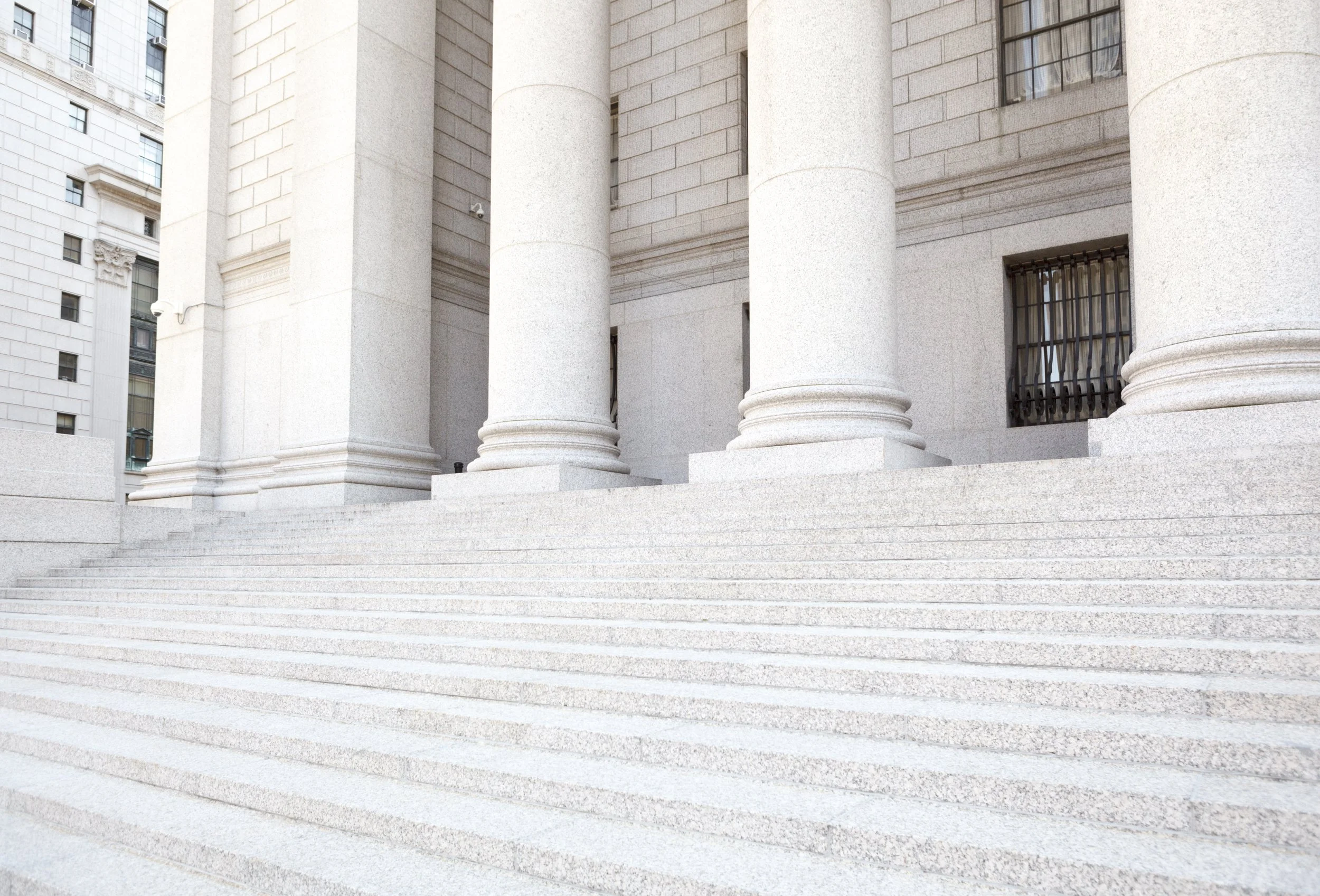 Stone steps leading up to a building with large columns and barred windows, part of a classical or government-style architecture.