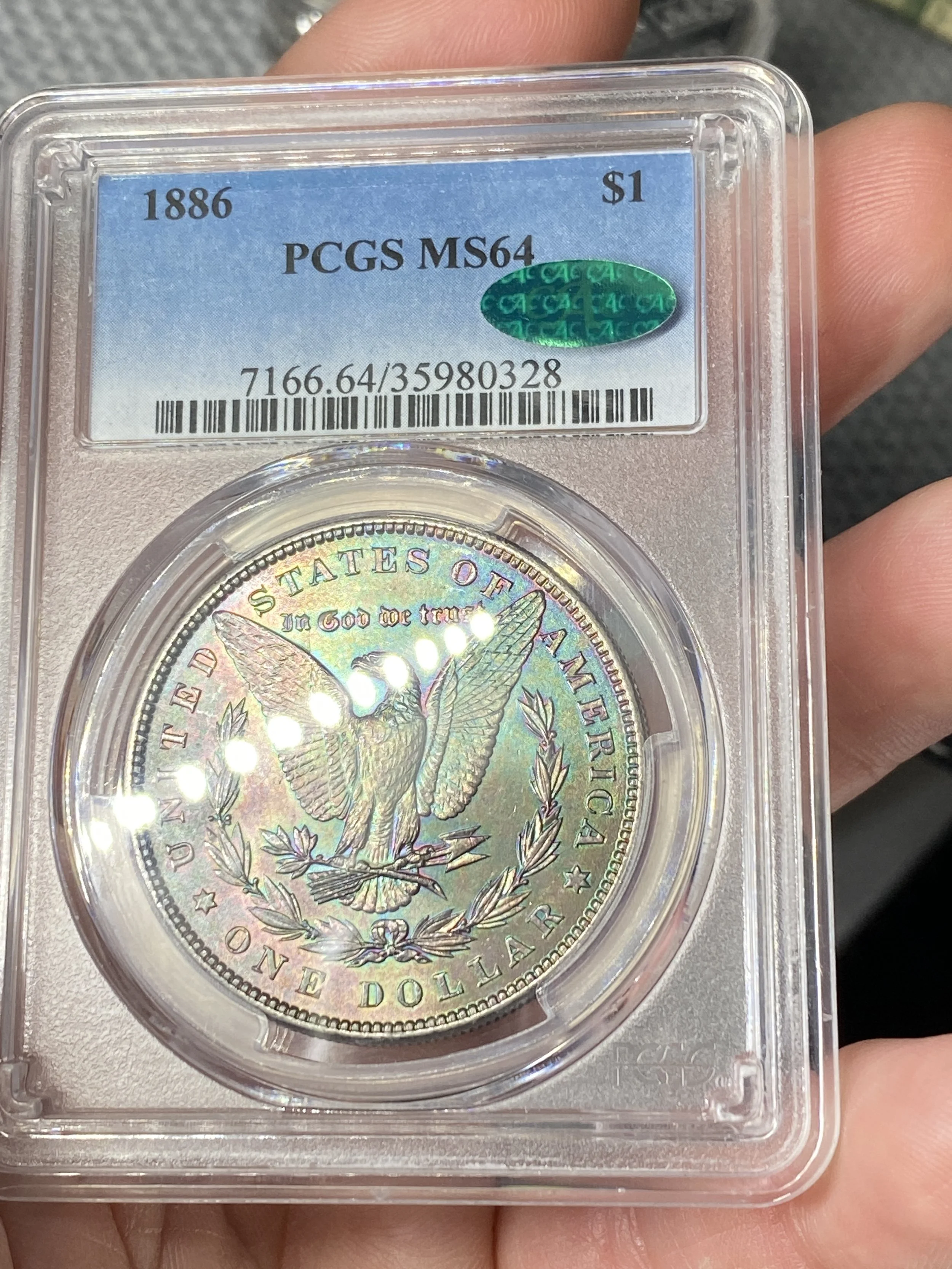 A graded 1886 Morgan silver dollar coin encapsulated in a clear plastic holder with a blue and white label, showing the coin's details such as grade MS64, denomination one dollar, and certification from PCGS.