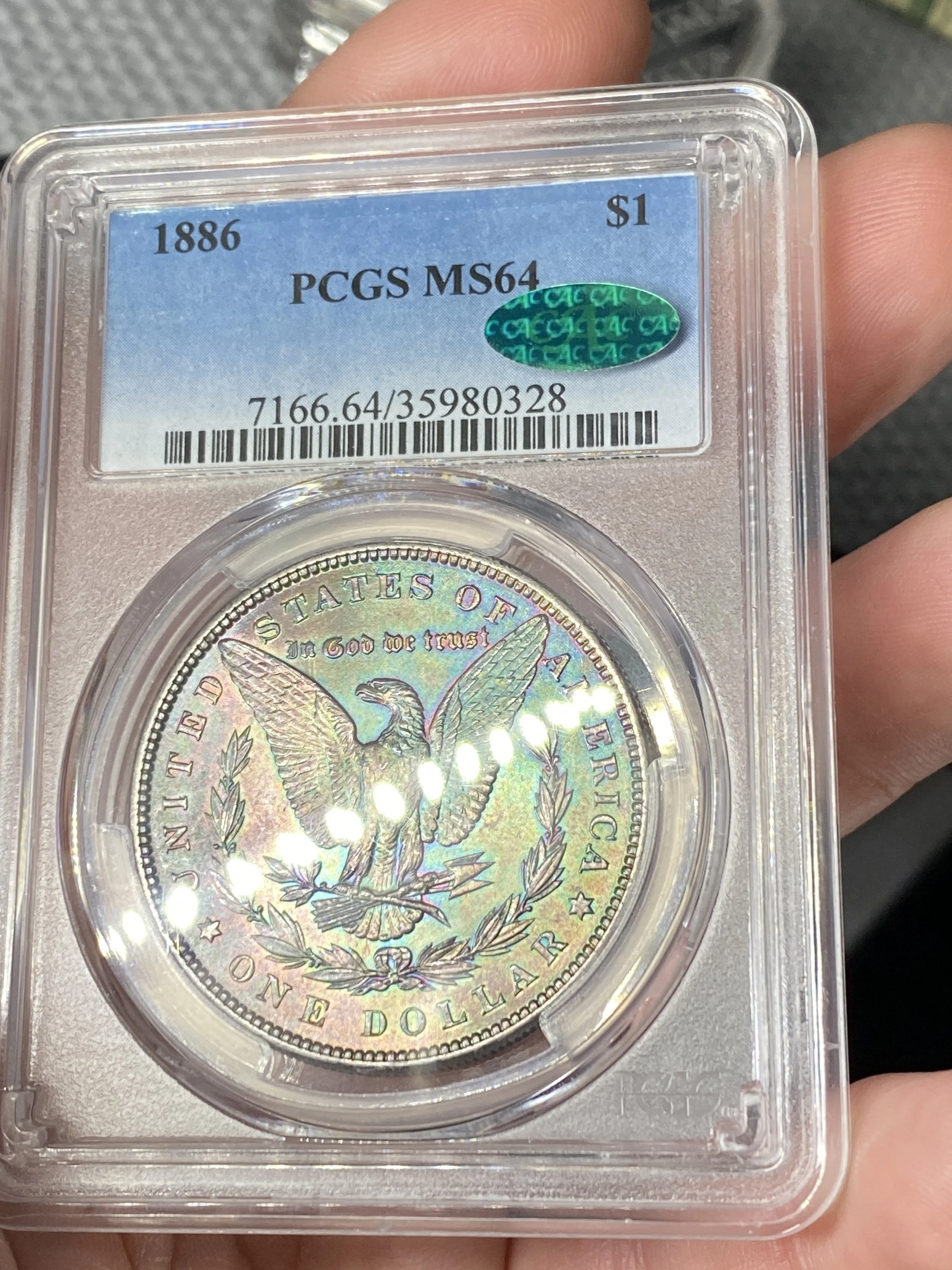 A 1886 Morgan Silver Dollar coin in a protective plastic holder, graded MS64, labeled by PCGS, with a blue and green holographic sticker, and a barcode, held in a person's hand.