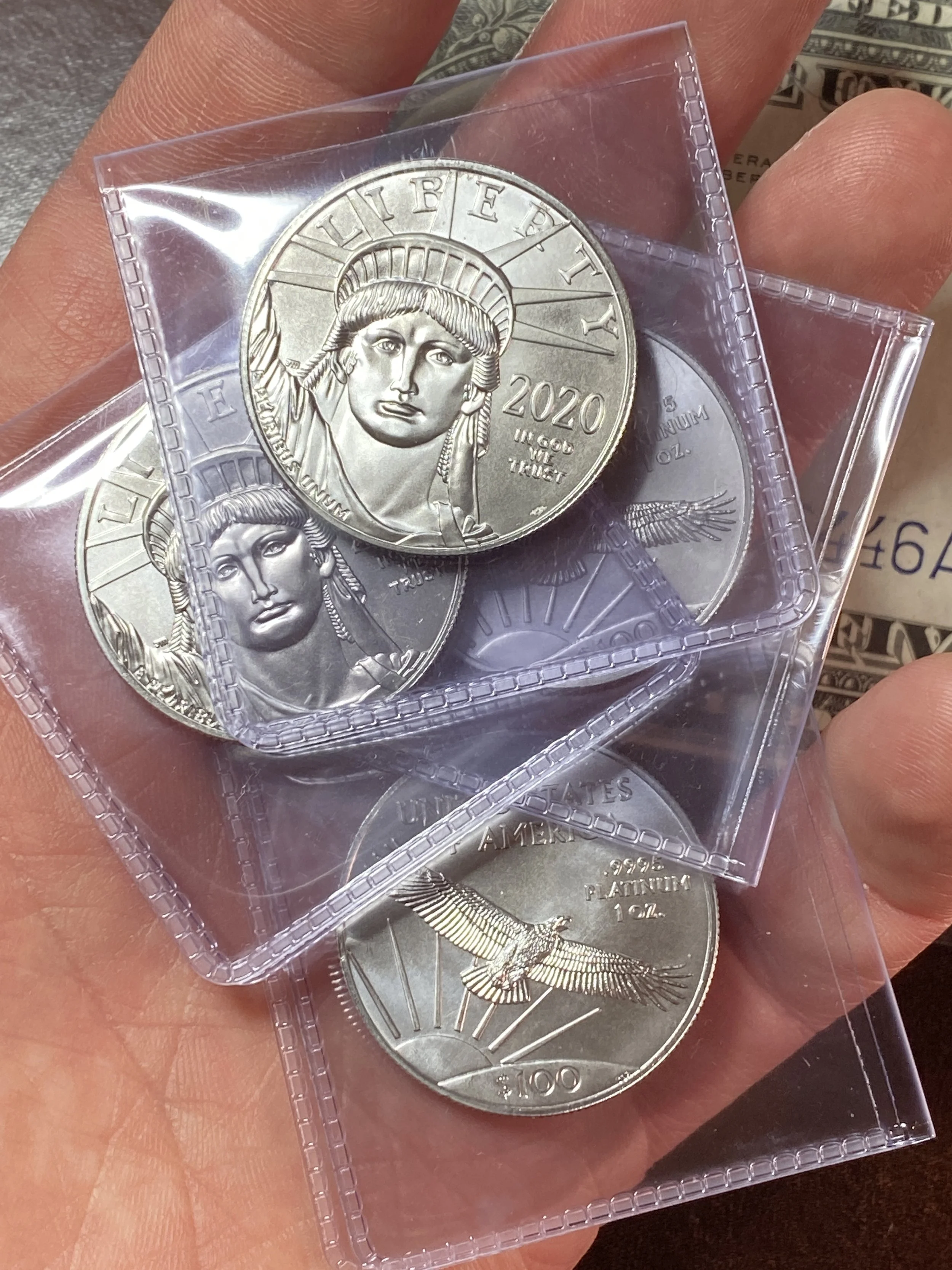 Multiple silver coins in plastic cases, featuring the Statue of Liberty's face, held in a person's hand.