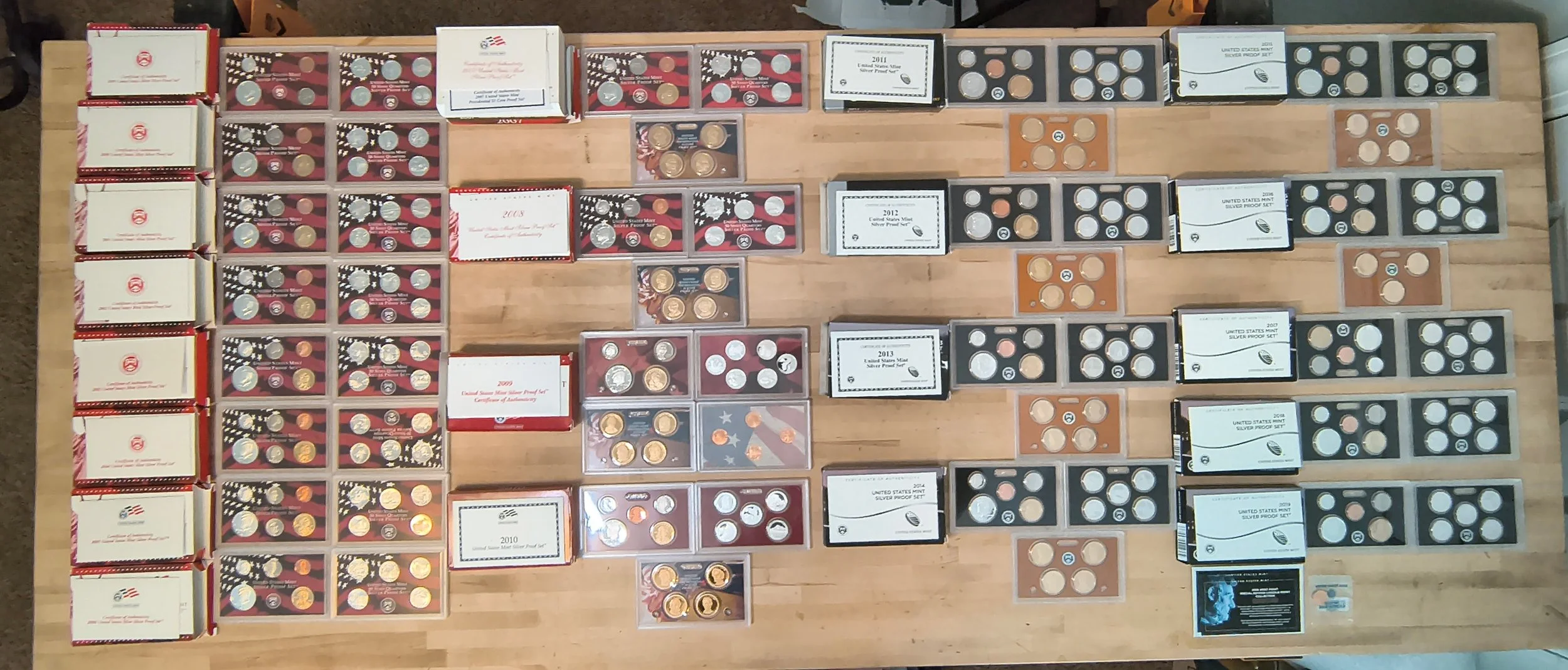 Collection of U.S. commemorative quarters and coin sets displayed on a wooden surface, organized by year and type.