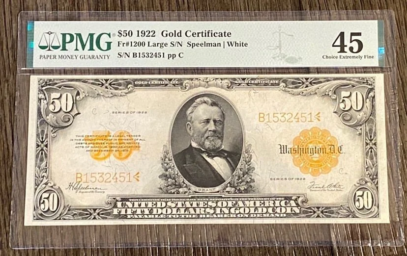 A $50 1922 gold certificate bill placed on a wooden surface, with a protective sleeve labeled PMG 45 Choice Extremely Fine.