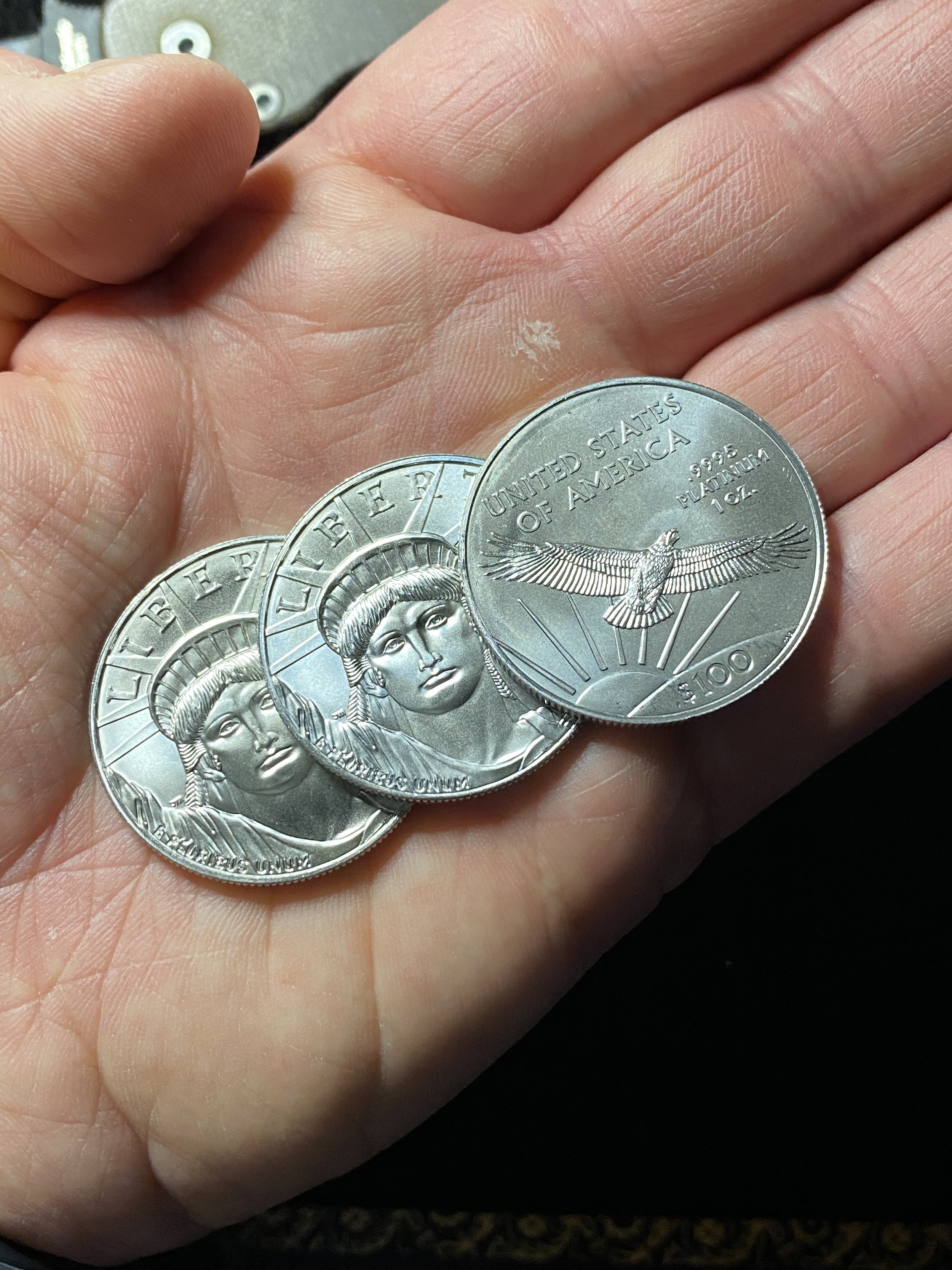 A person's hand holding three U.S. silver coins with the image of a Native American on the front and an eagle on the back.