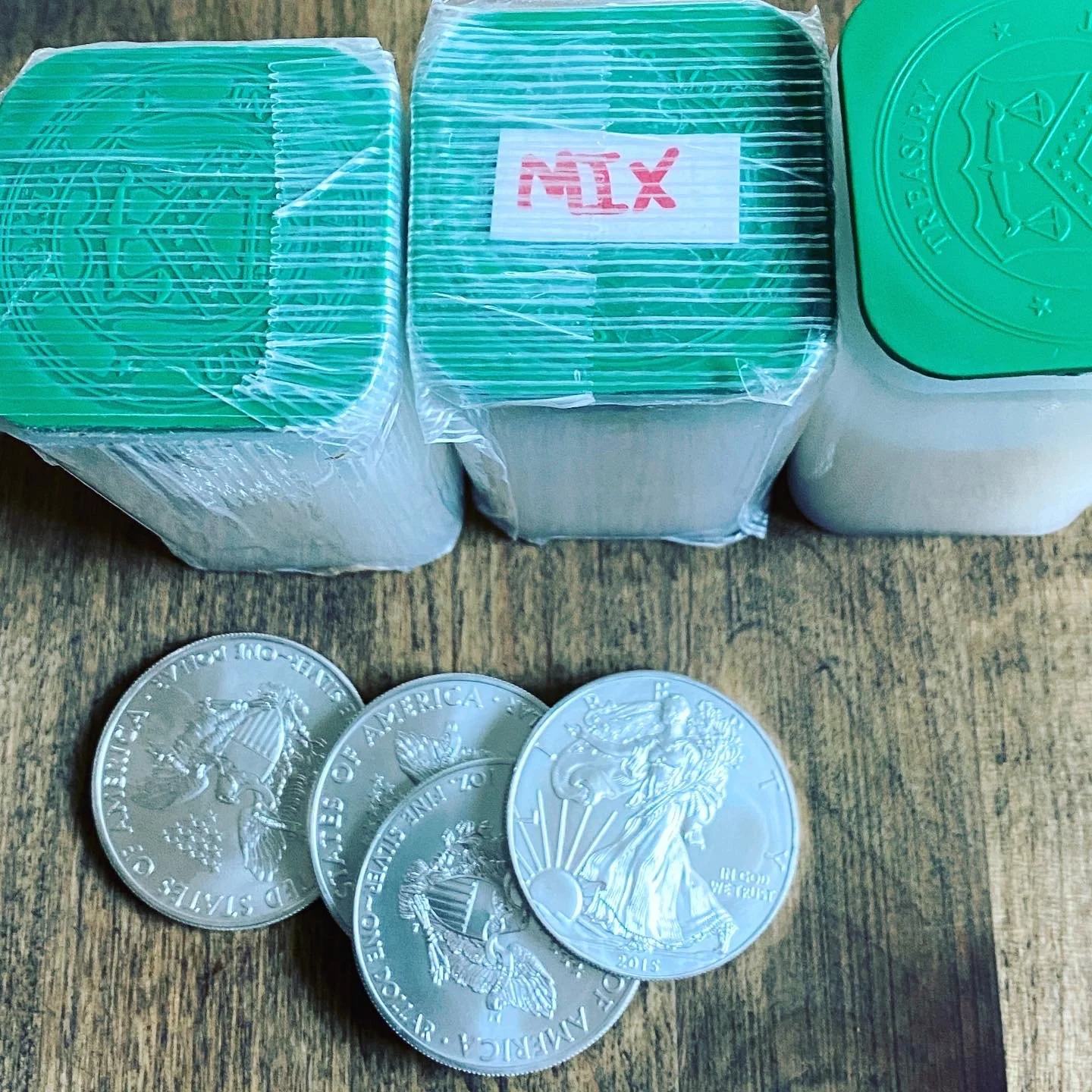 Three packs of chewing gum with plastic wrapping and three quarters in front of the packs on a wooden surface.