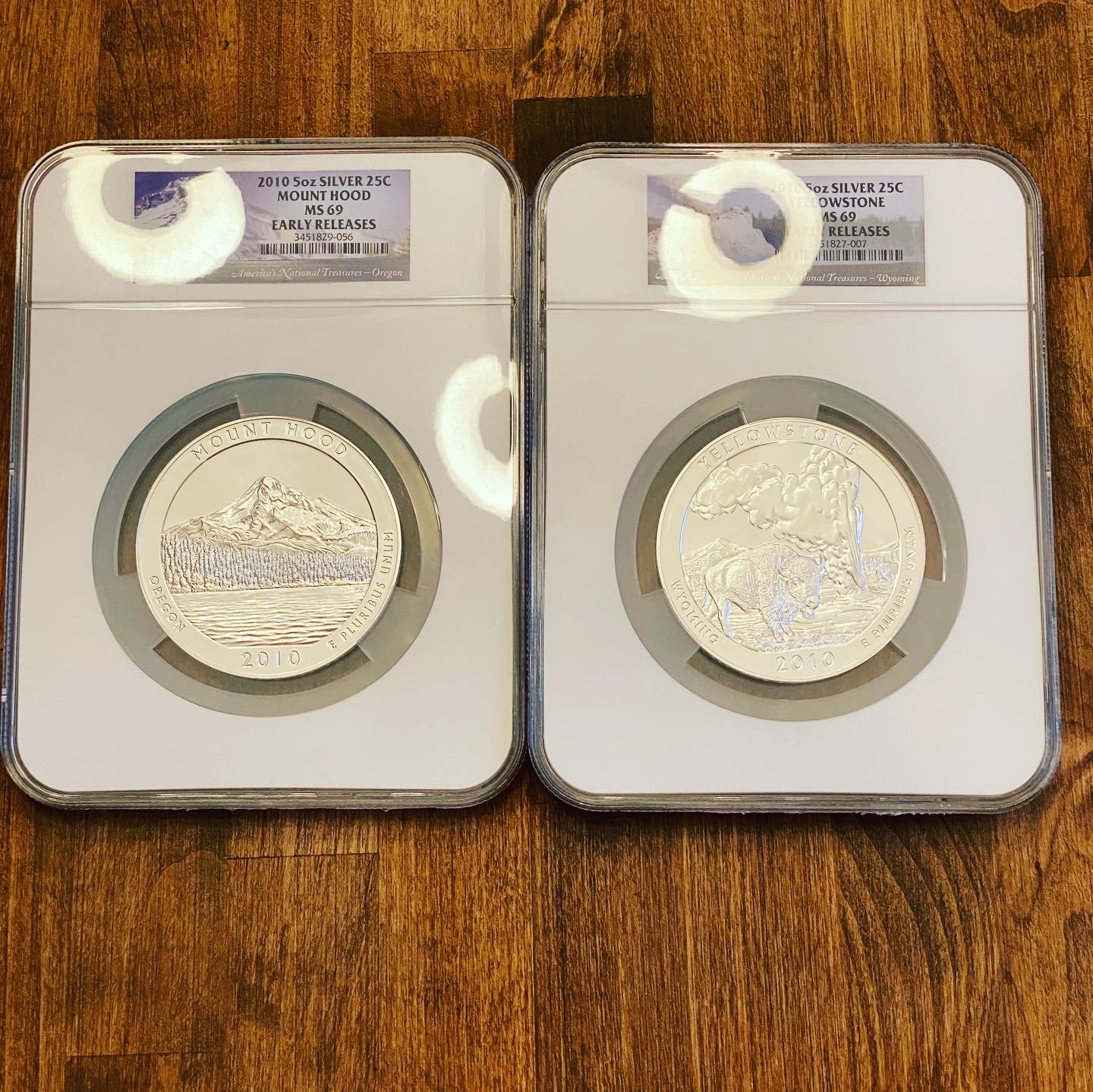 Two coin slabs with Silver coins from 2010, Mount Hood and Yellowstone. The Mount Hood coin features a mountain view, and the Yellowstone coin depicts a bison and geothermal activity.