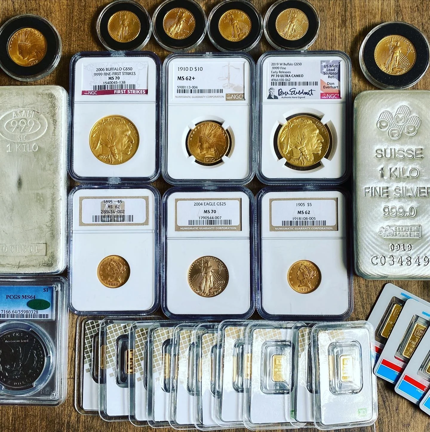 A collection of gold and silver coins, including American gold coins with various dates and denominations, some graded and encapsulated, along with silver bars and coins, displayed on a wooden surface.