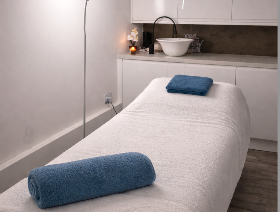 Spa or massage therapy room with a massage table covered in white towel, two folded blue towels, and a minimalistic decor with a sink, sink faucet, orchid plant, and candles.