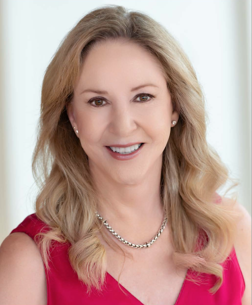 A kind businesswoman with blonde hair, wearing a red sleeveless top, smiling at the camera.
