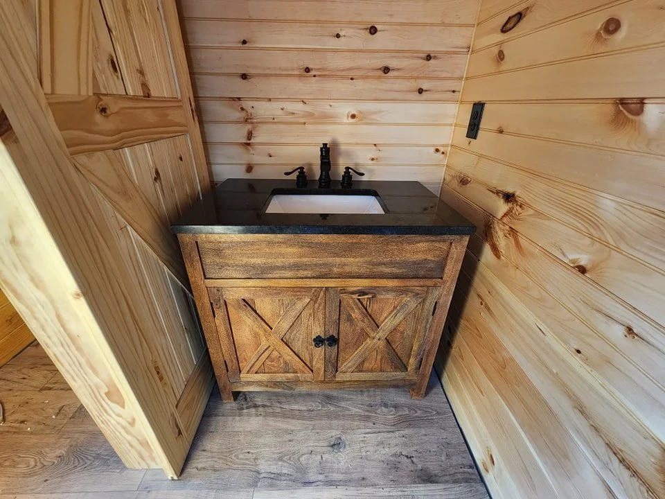 Wooden bathroom vanity with a black countertop and a small white sink, situated in a wooden-paneled room.