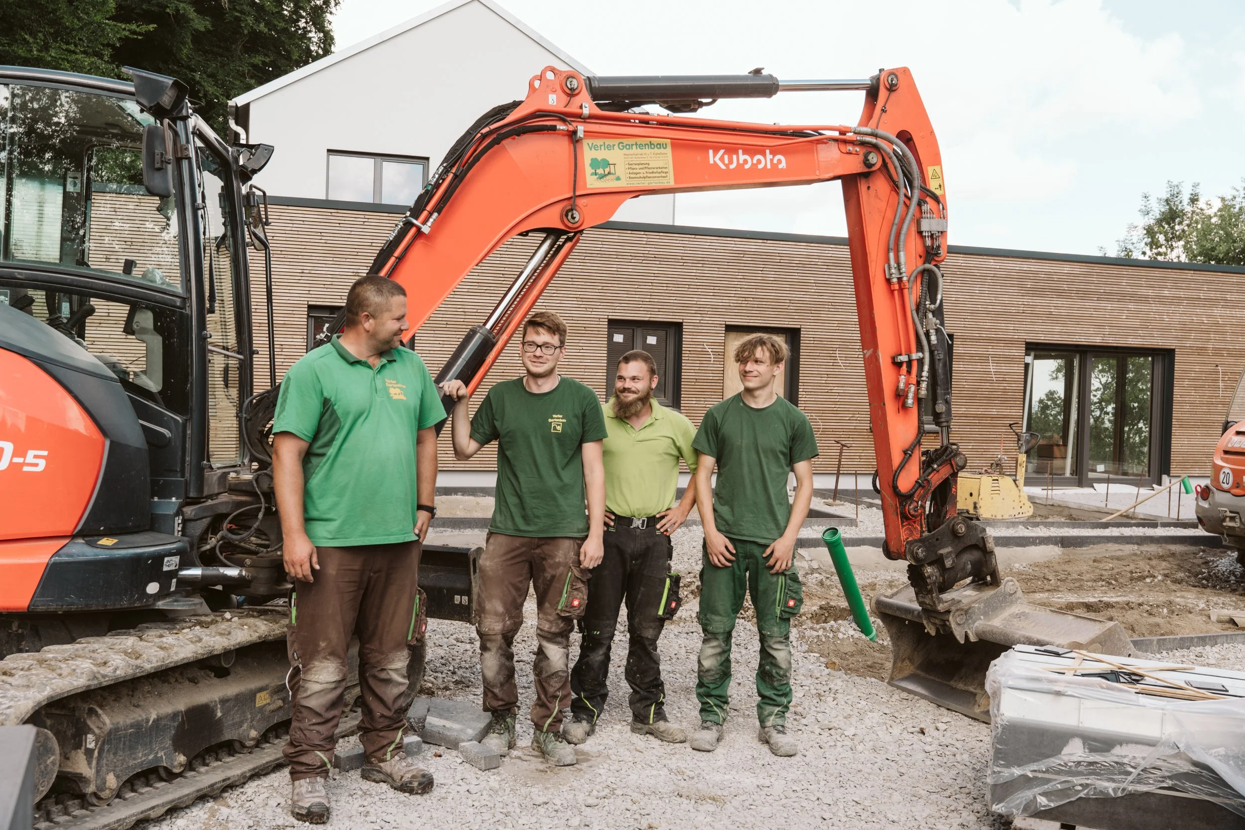 Four men standing in front of construction equipment outdoors, with a building in the background.