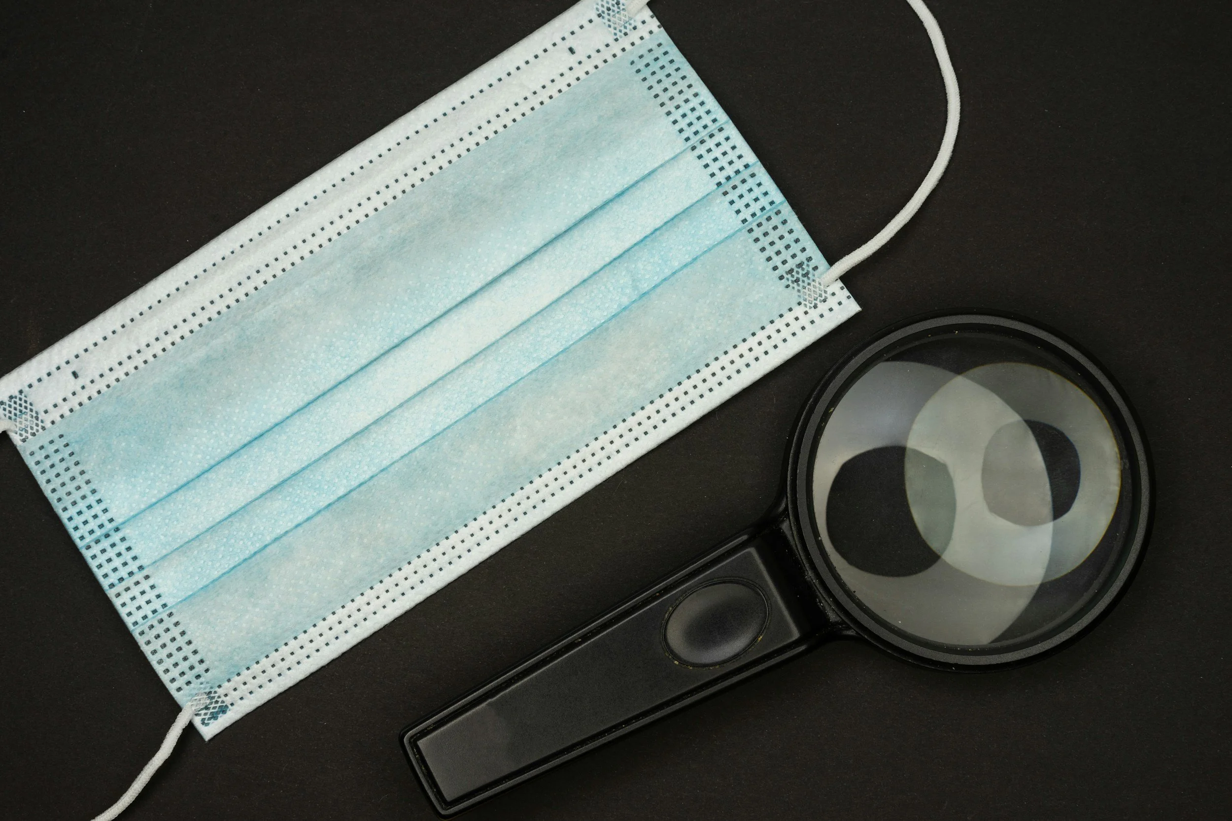 Una mascarilla de color azul, un recipiente con lentes de protección y un recipiente con filtros de protección, colocados sobre una superficie negra.
