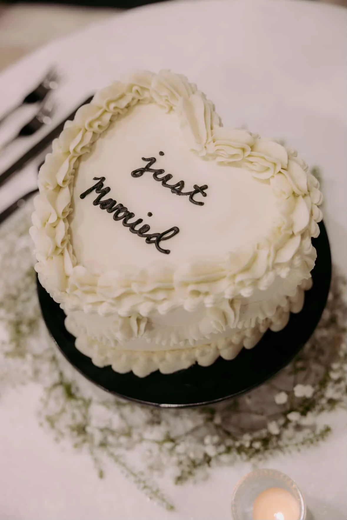 White heart-shaped cake with decorative frosting border, inscribed with 'just married' in black icing, on a black serving plate.